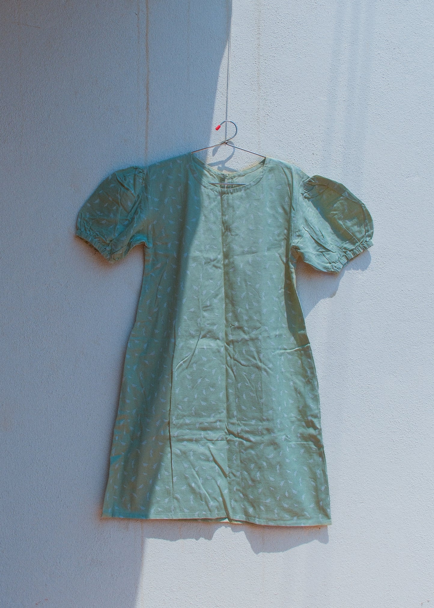 sage green cotton-linen mini dress on a hanger against a white wall