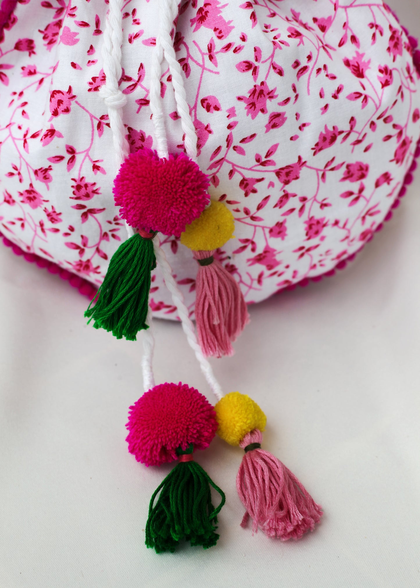 Floral print drawstring bag with colorful pom-pom tassels on a white background