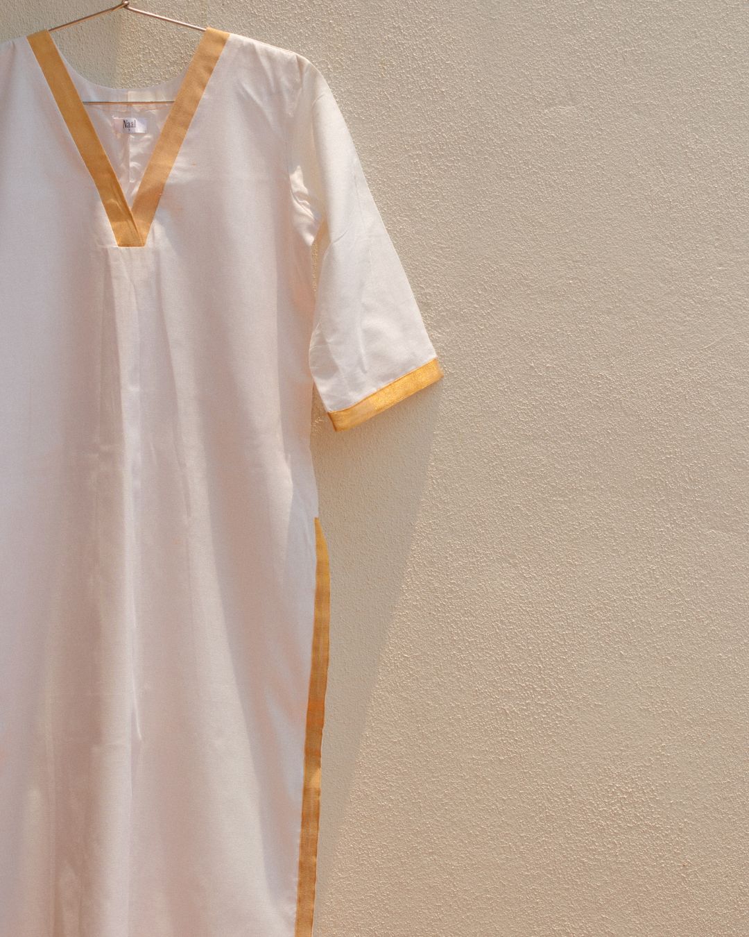 White cotton kurta with gold zari border on a beige wall