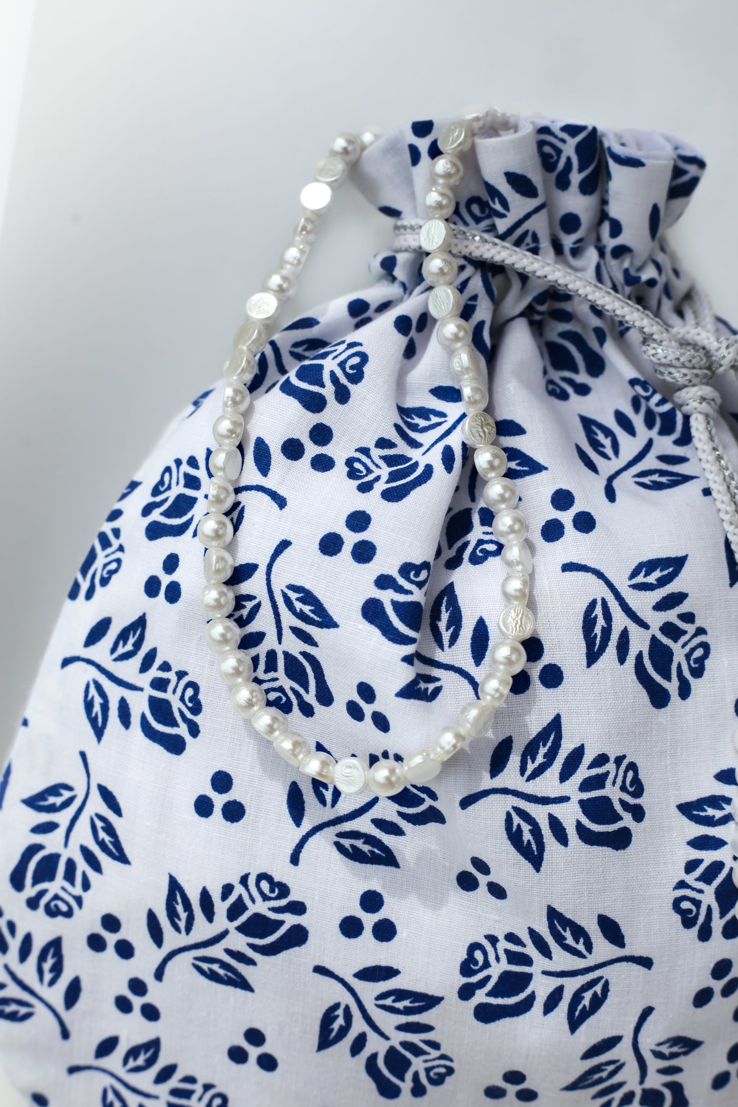 Pearl handle of cotton drawstring bag with blue floral patterns on a white background