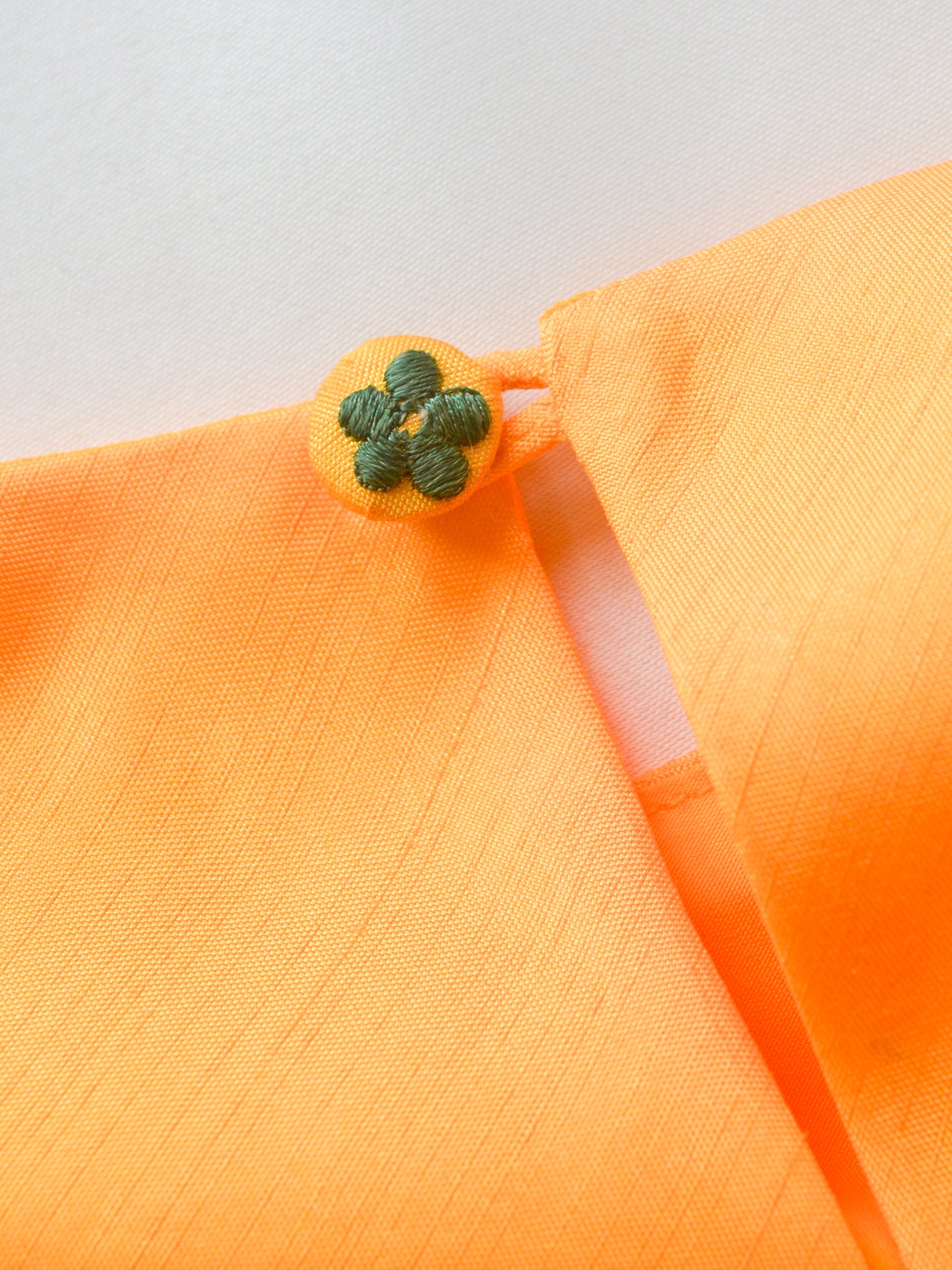 Close-up of the flower motif embroidered on fabric button on the back of the yellow muslin silk shevanti kurta.