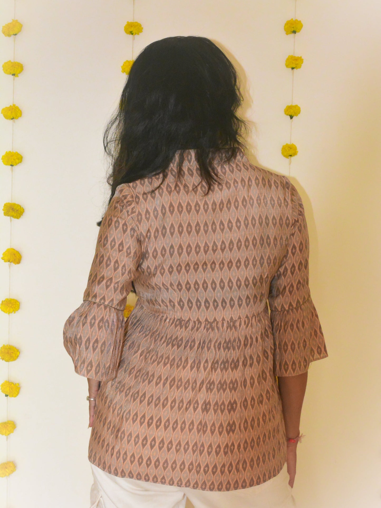Woman wearing a beige printed musli-silk tunic with a neutral background and yellow decorative flowers.