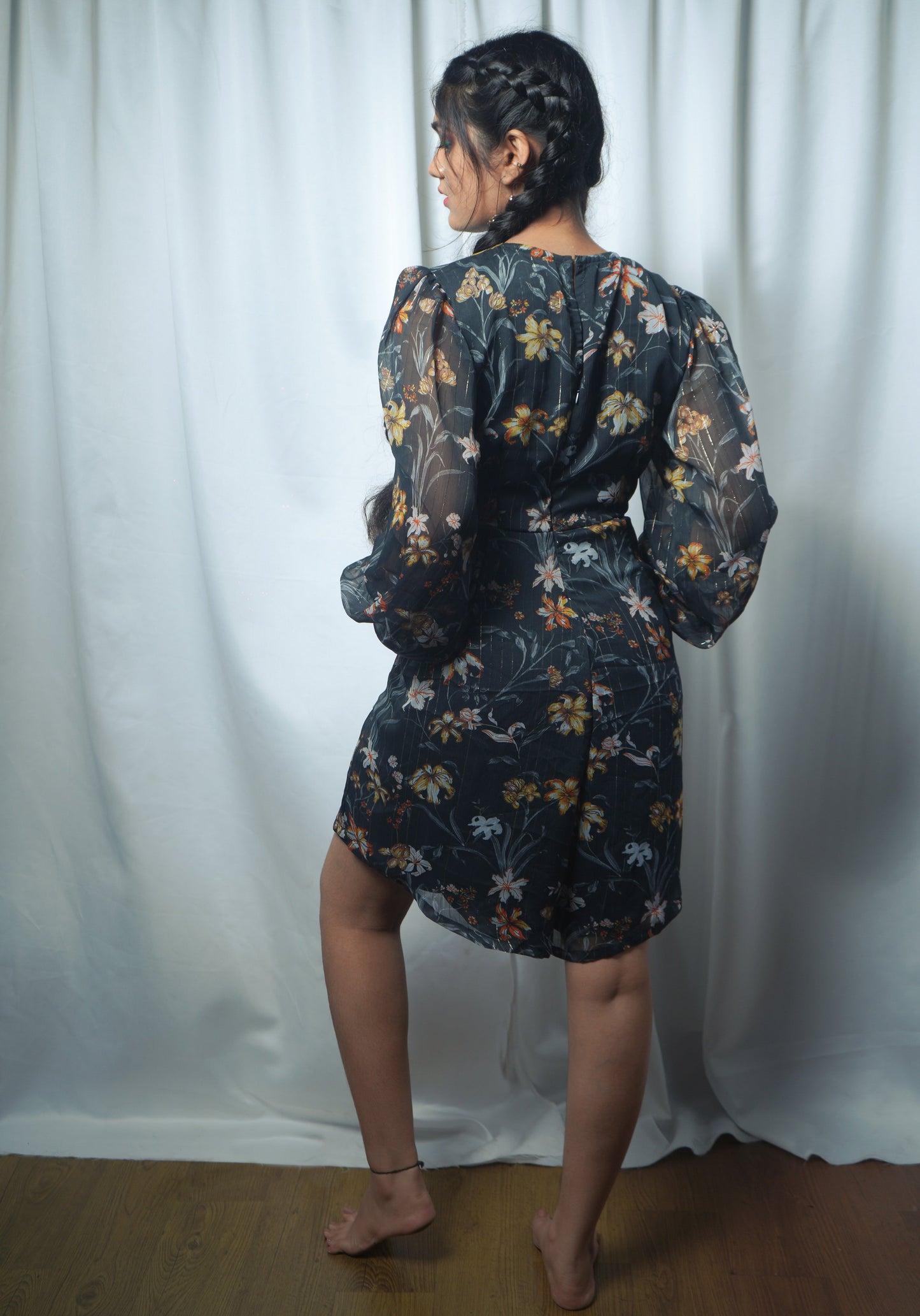 Person wearing a black floral playsuit standing against a white curtain