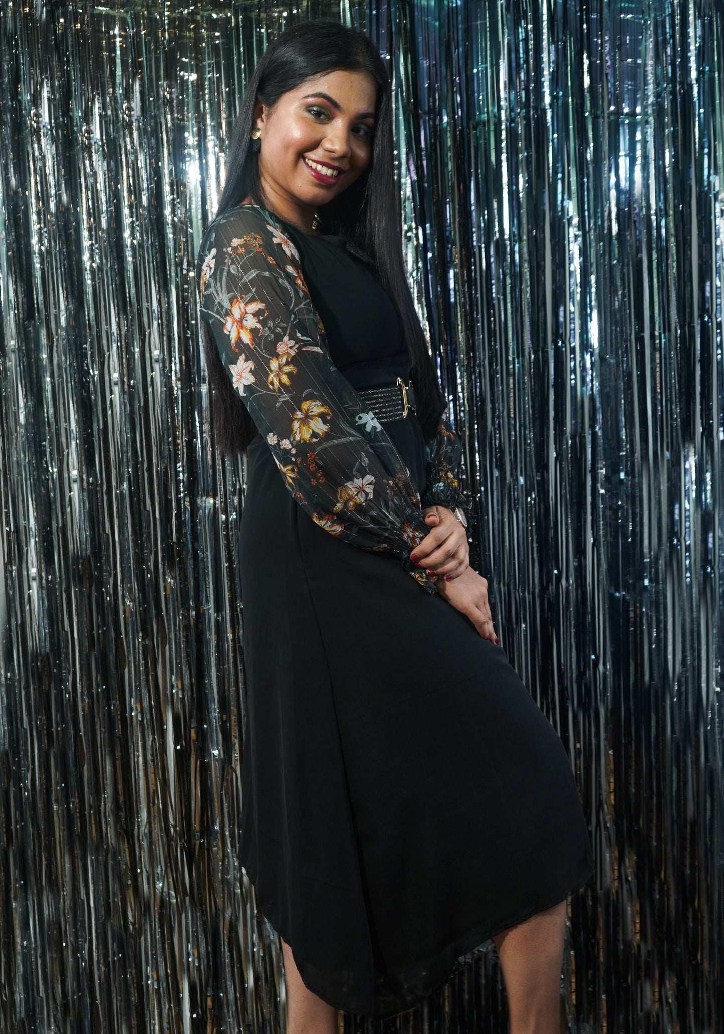 A woman wearing an asymmetrical knee length dress with floral printed long sleeves and a scoop neckline in a charcoal black color