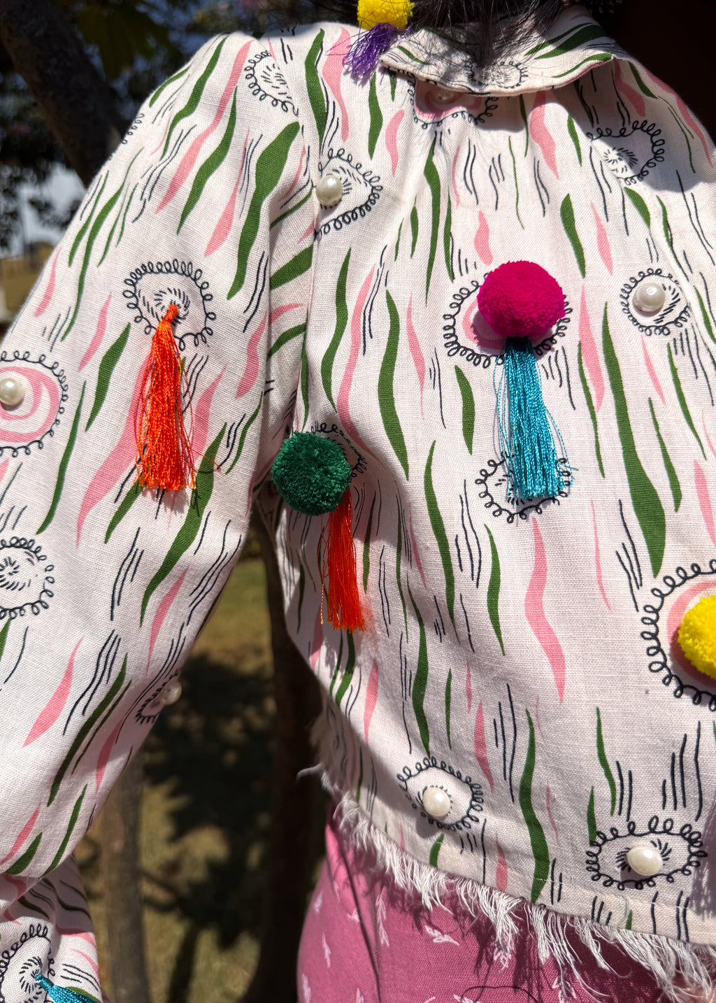 Close-up of vibrant tassels and pompoms on front and long sleeves of the off-white cotton Bubblegum Pop Cropped Jacket.