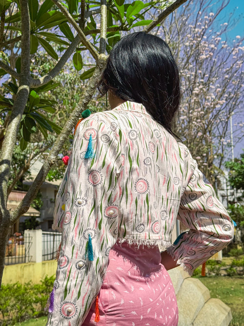 Back view of the off white cotton Bubblegum Pop Printed cropped jacket, showing vibrant tassels, pom-poms, and fringed hemline, paired with Cotton Candy Slip Dress.