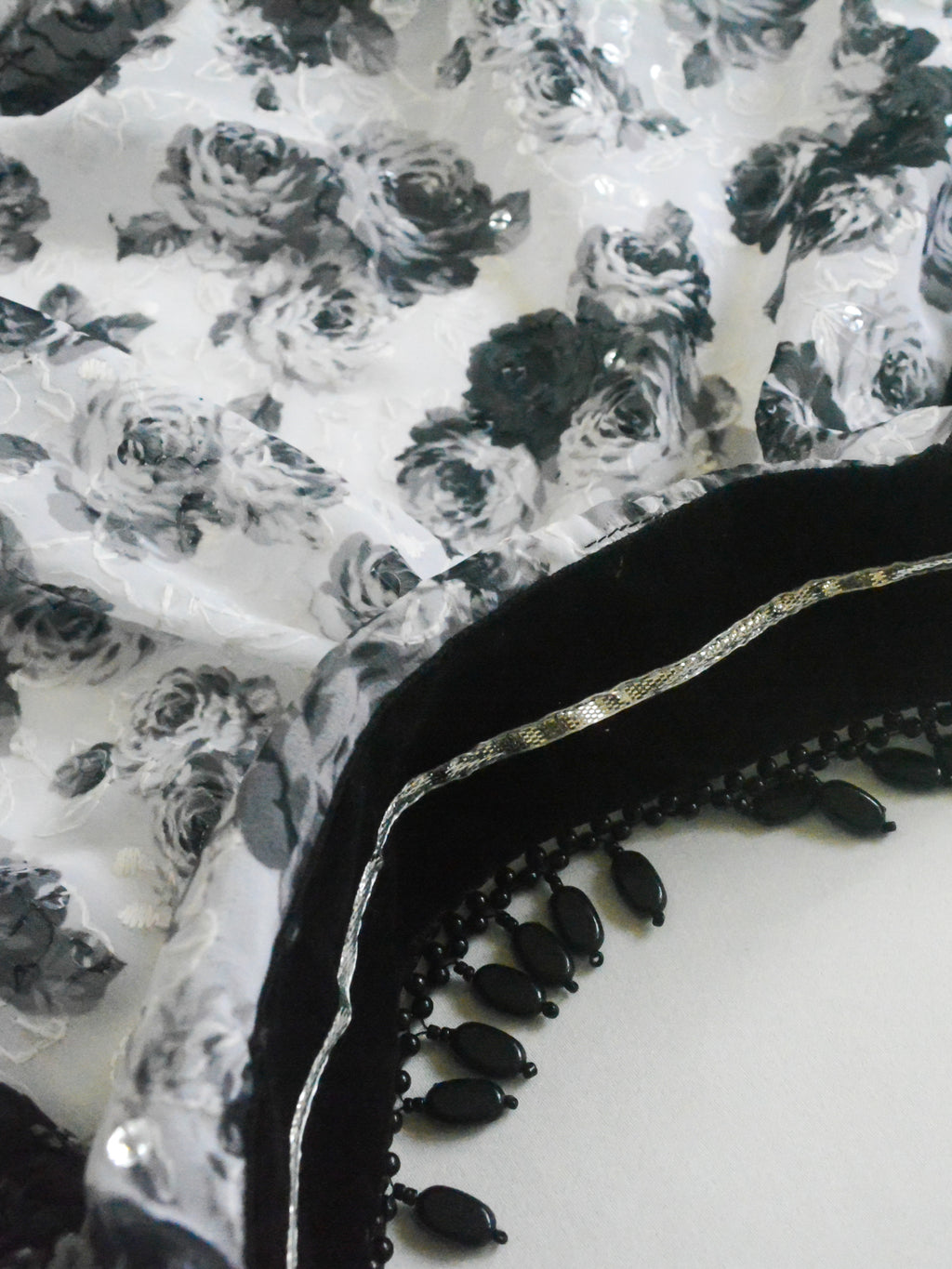 Close-up of a Guldasta Saree showing a classic black and white rose print, intricate self-tone white embroidery, and subtle transparent sequins, with a black velvet and silver gotta patti border.
