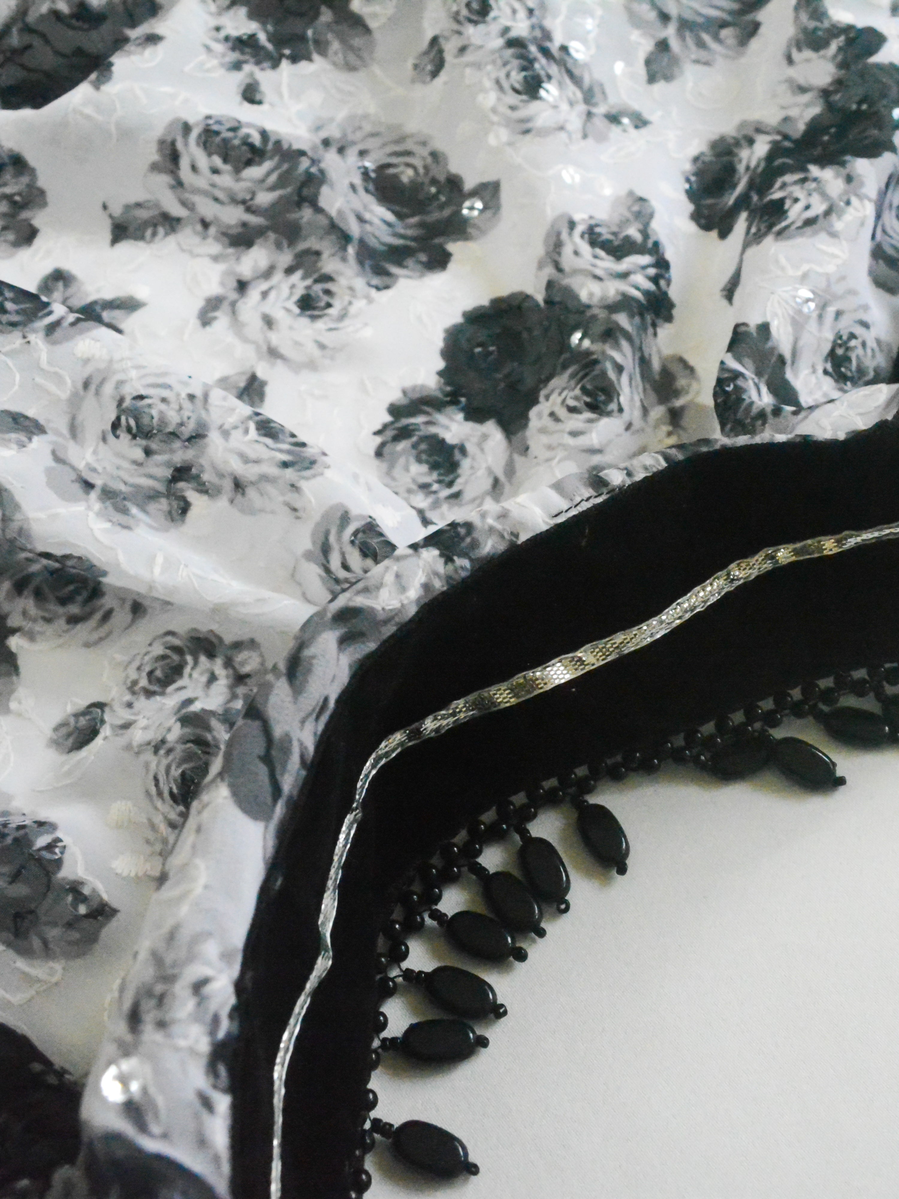 Close-up of a Guldasta Saree showing a classic black and white rose print, intricate self-tone white embroidery, and subtle transparent sequins, with a black velvet and silver gotta patti border.