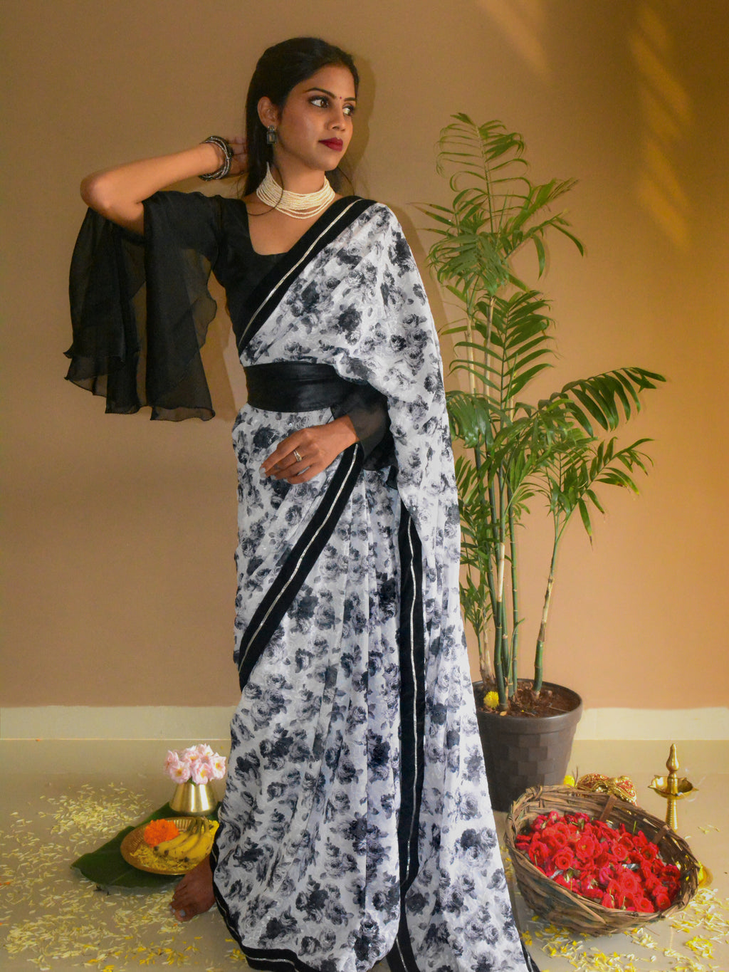 Model wearing a printed Guldasta Saree featuring a rose print in black and white, black velvet border with silver gotta patti, and scattered transparent sequins, evoking a retro 1980s vibe. The saree is paired with black blouse in cotton-silk, flared embroidered sleeves. Styled with wide leather belt, and Ratnarani Beaded Choker.