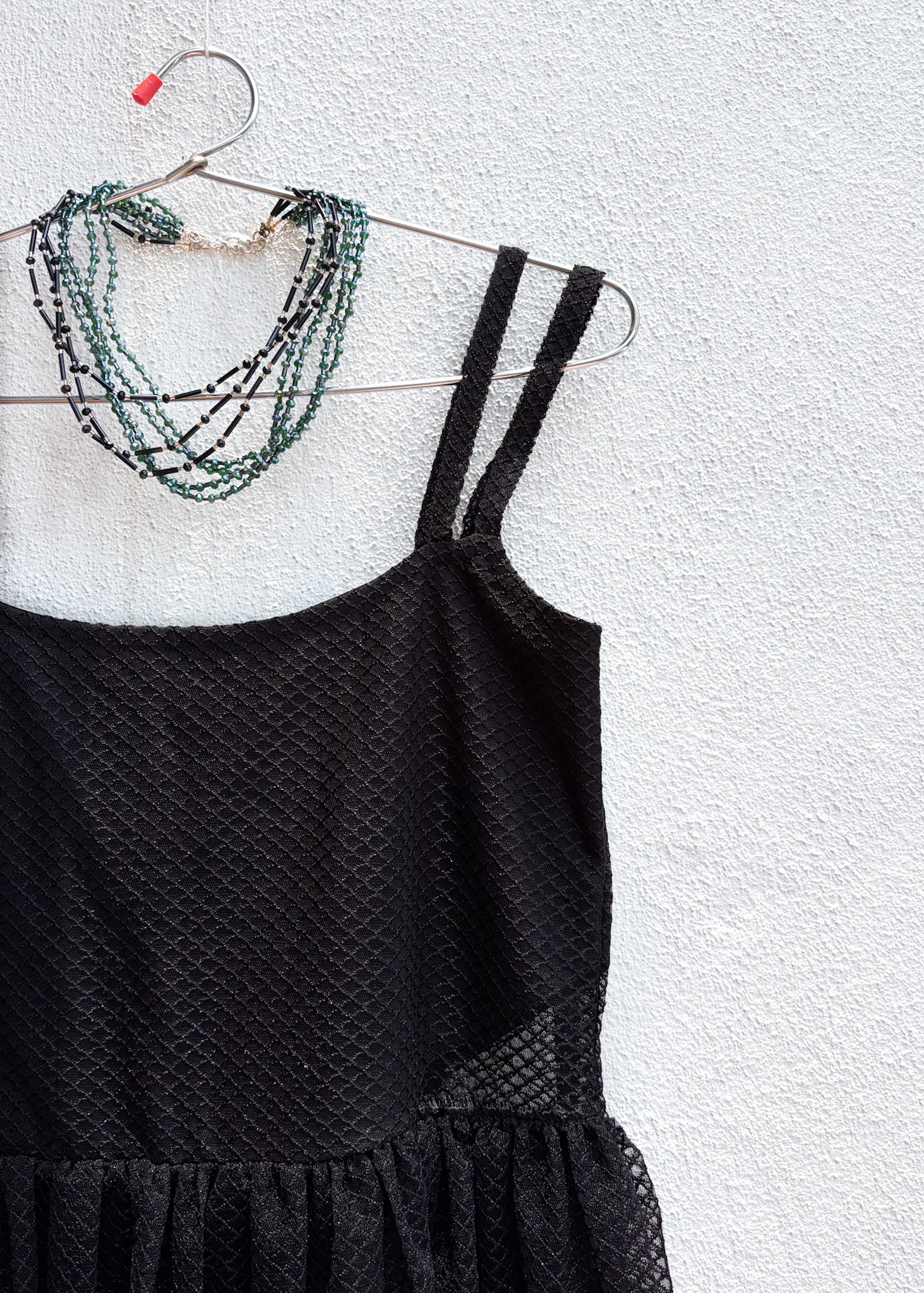 Black tulle dress yoke with thin straps, and layered necklaces on a hanger against a light gray background.