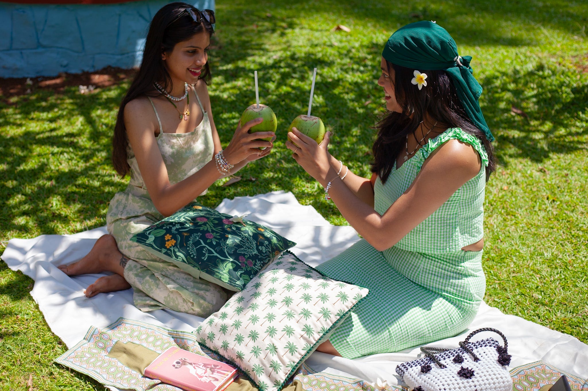Two women sitting on a blanket in a park, enjoying drinks.