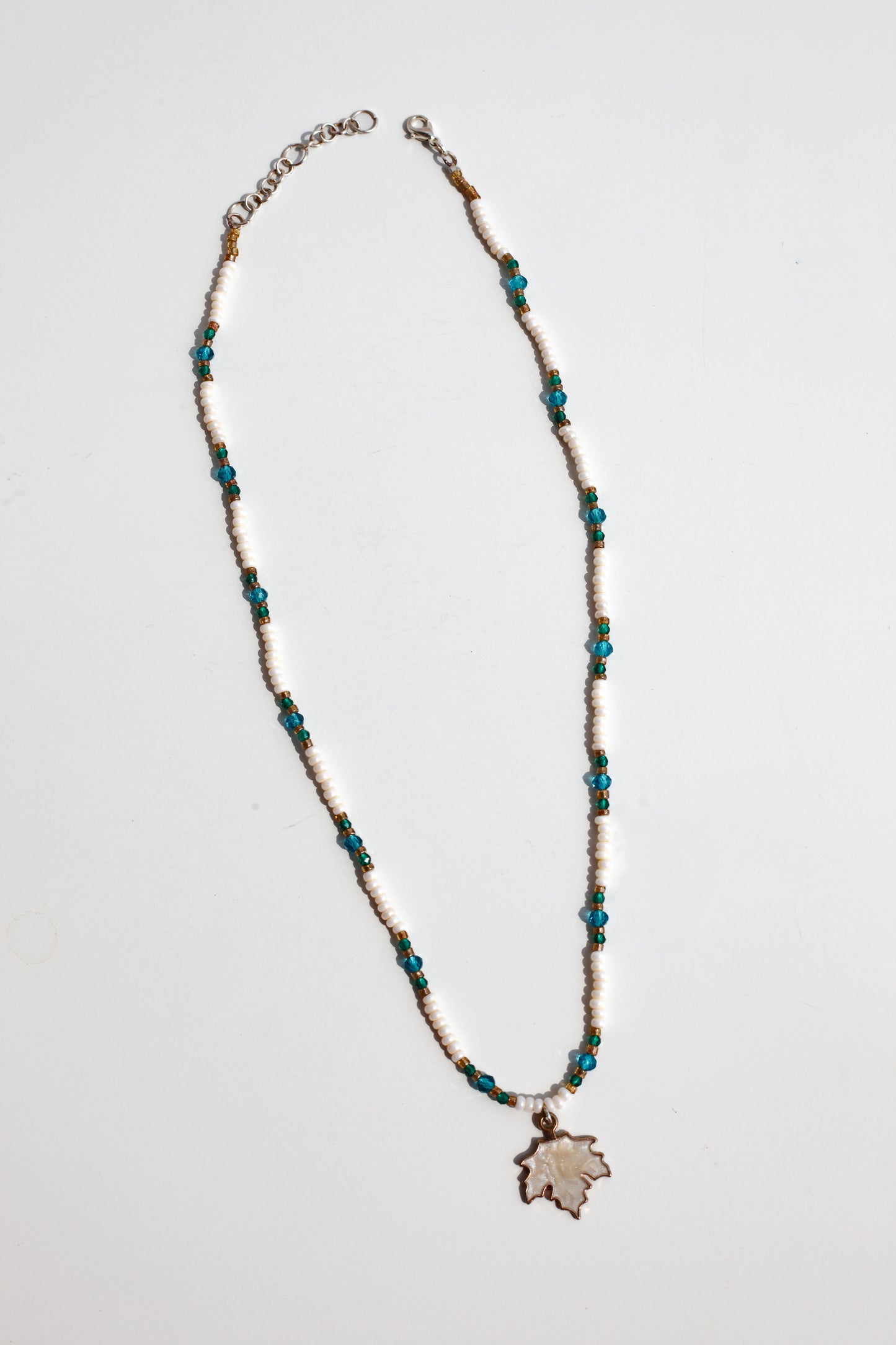 Necklace with blue beads and a autumn leaf-shaped pendant on a light gray background