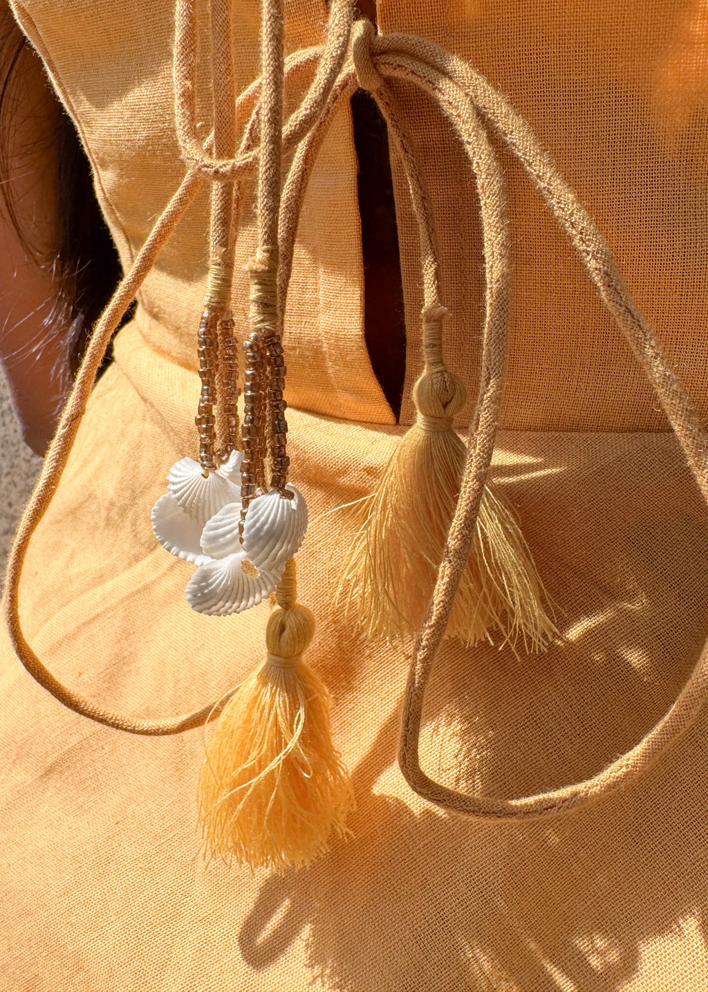 Back view of the yellow cotton-linen Sandshells Dress showing the shells and tassel tie-up detail.