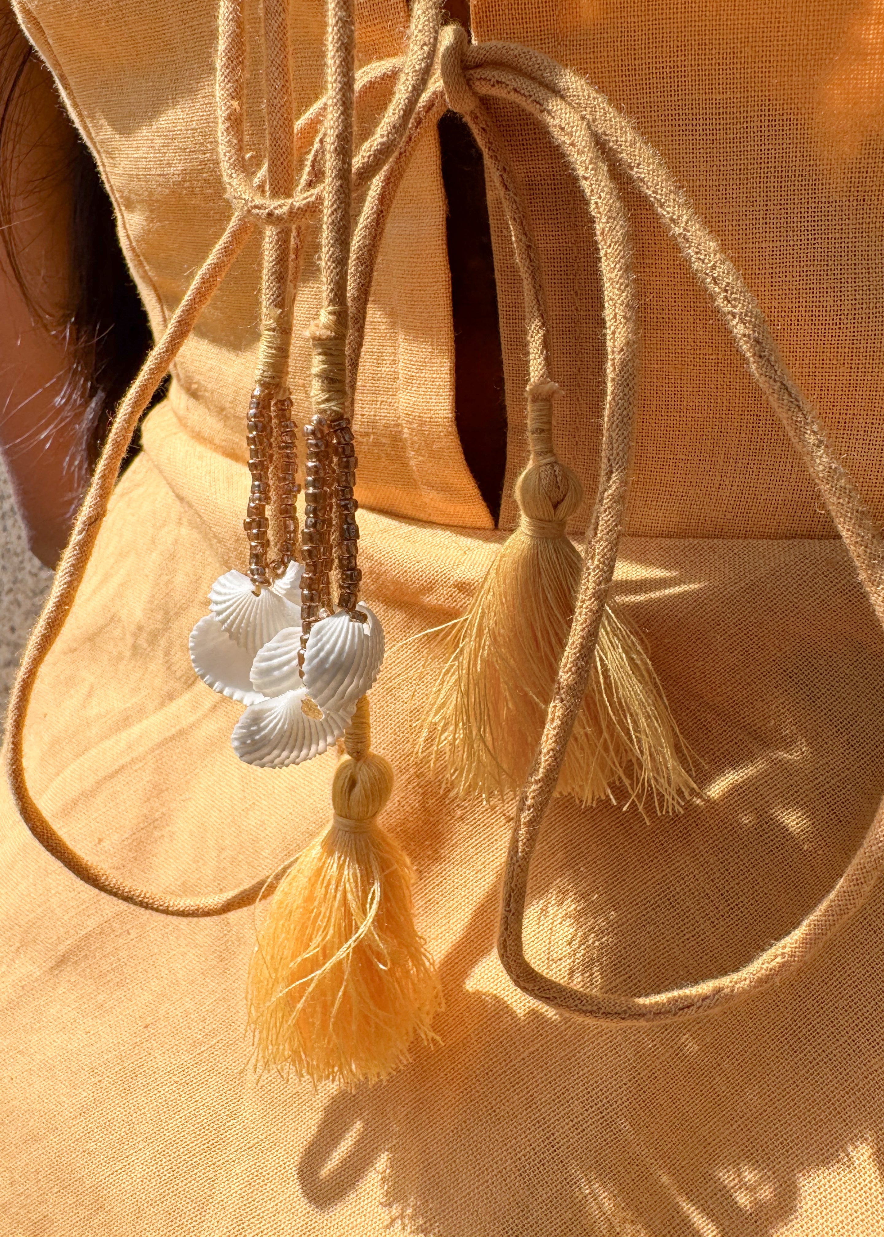 Back view of the yellow cotton-linen Sandshells Dress showing the shells and tassel tie-up detail.