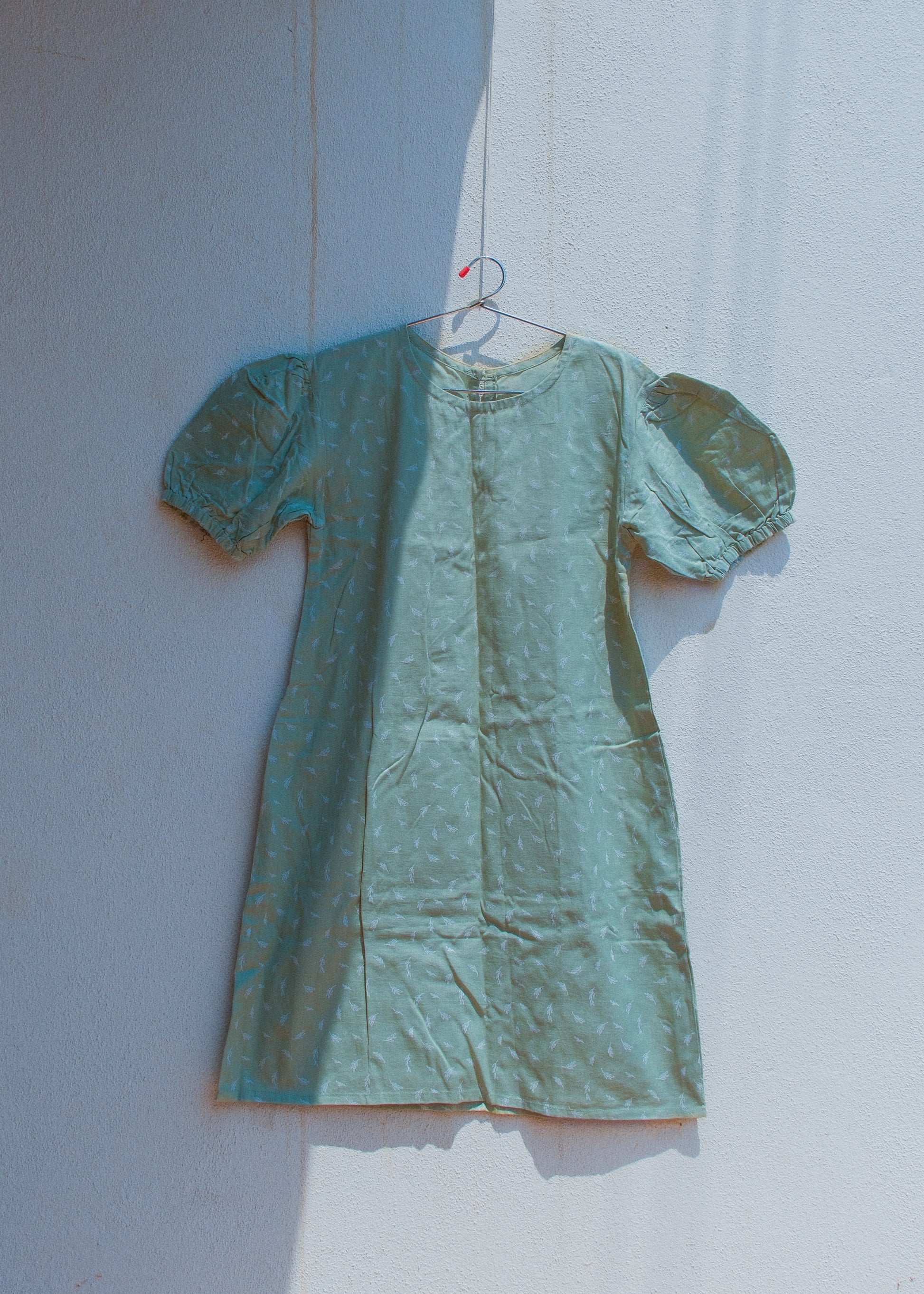 sage green cotton-linen mini dress on a hanger against a white wall