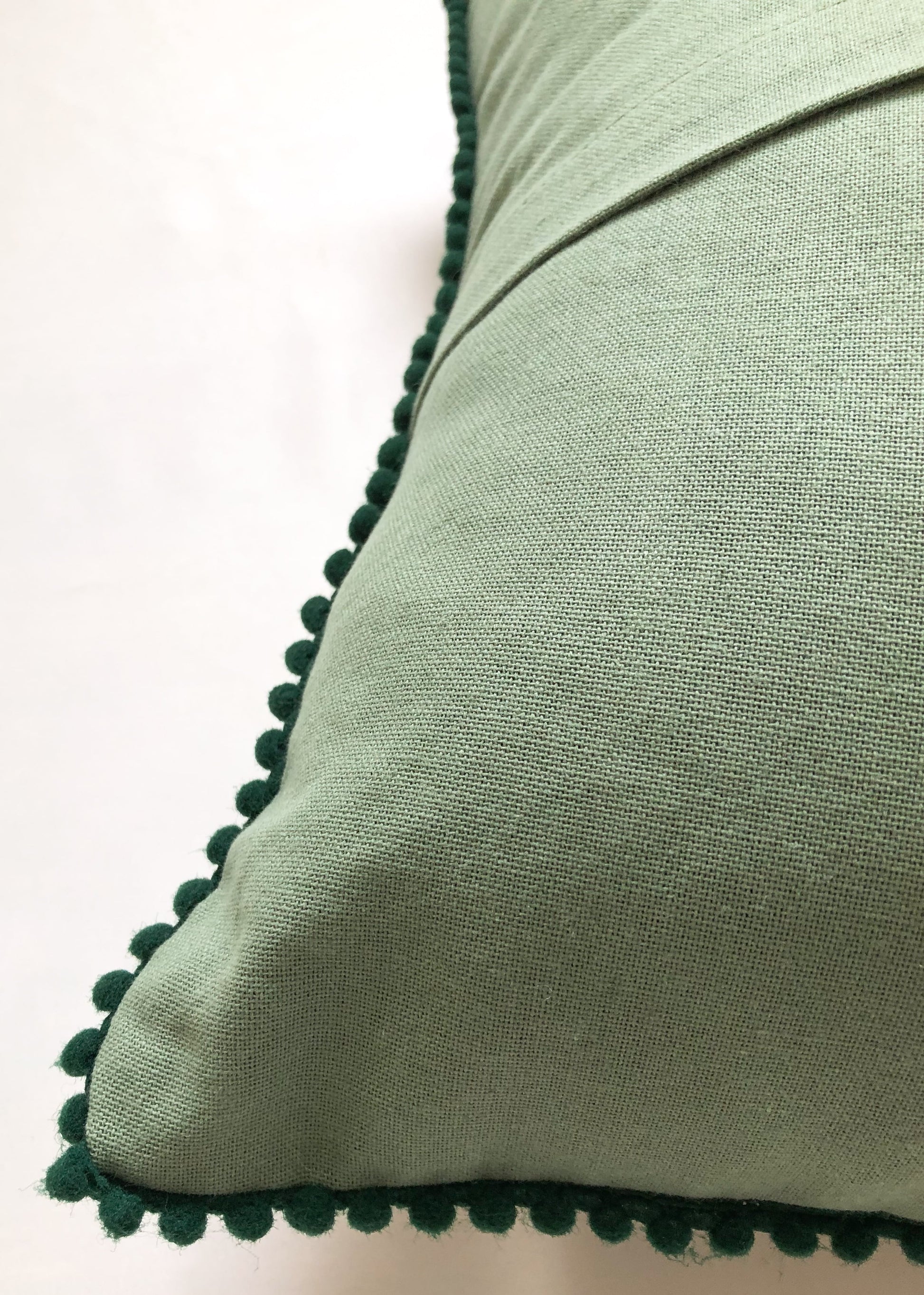 Close-up of pompom lace on a green cotton cushion cover. Handcrafted detailing texture for a luxurious touch.