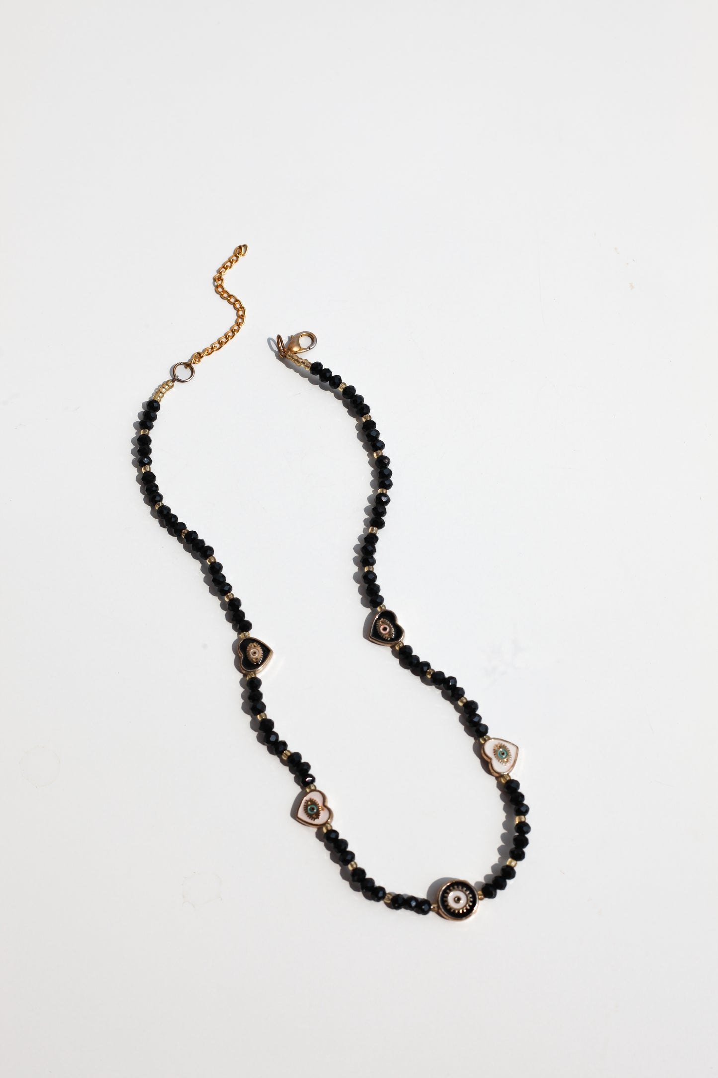 Necklace with black beads, evil eye charms, and gold accents on a light gray background