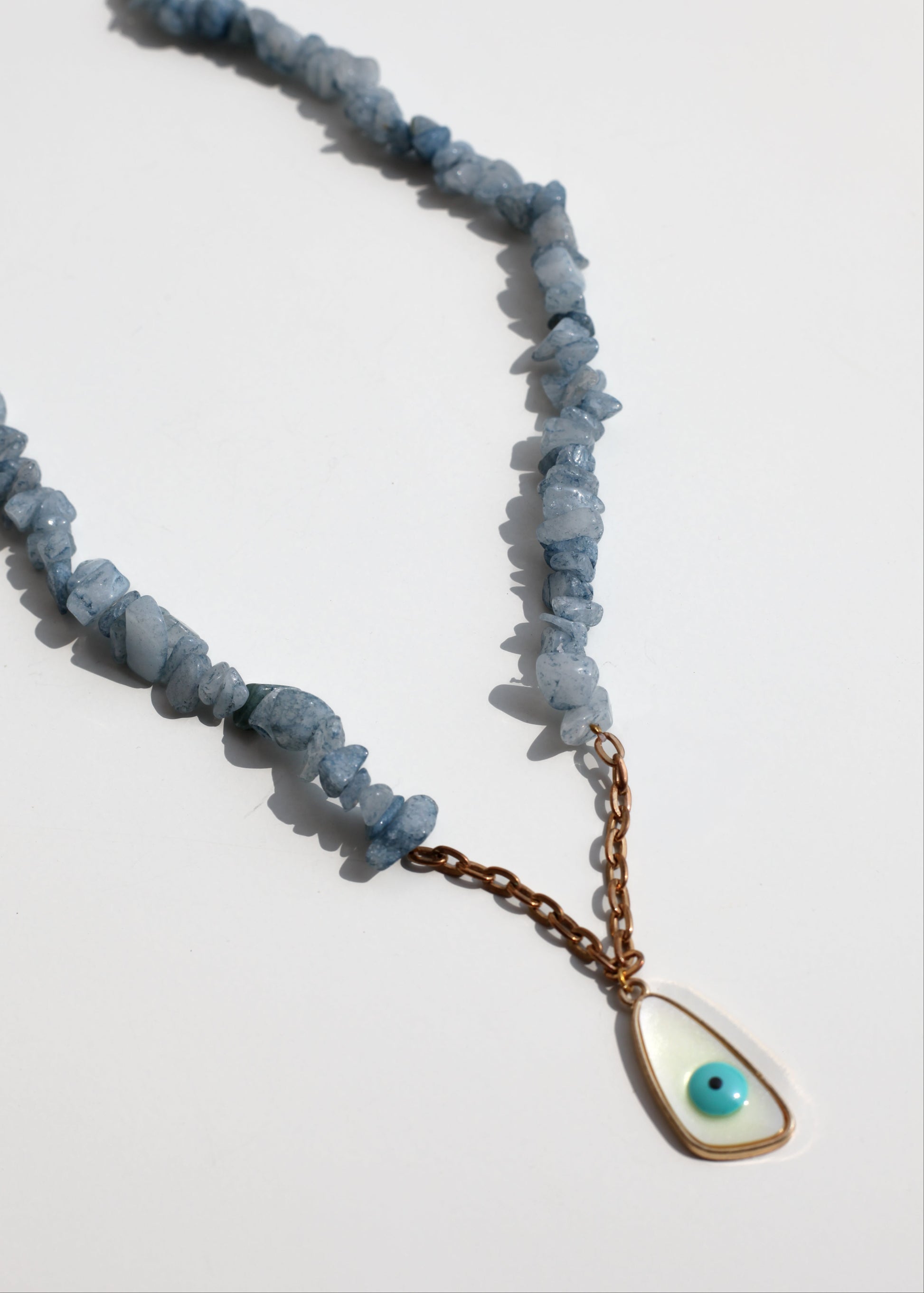 Necklace with blue stone beads and a gold teardrop pendant on a white background