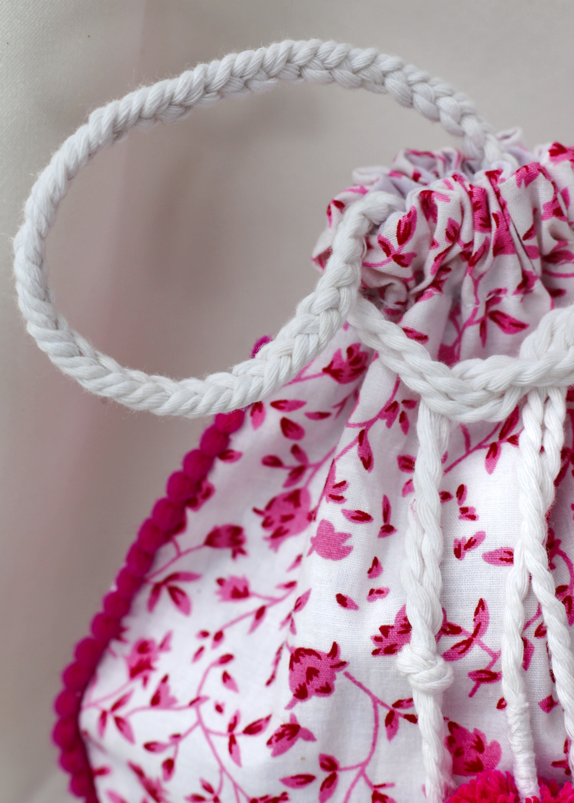 Close-up of a drawstring bag with pink floral pattern and white braided handle.