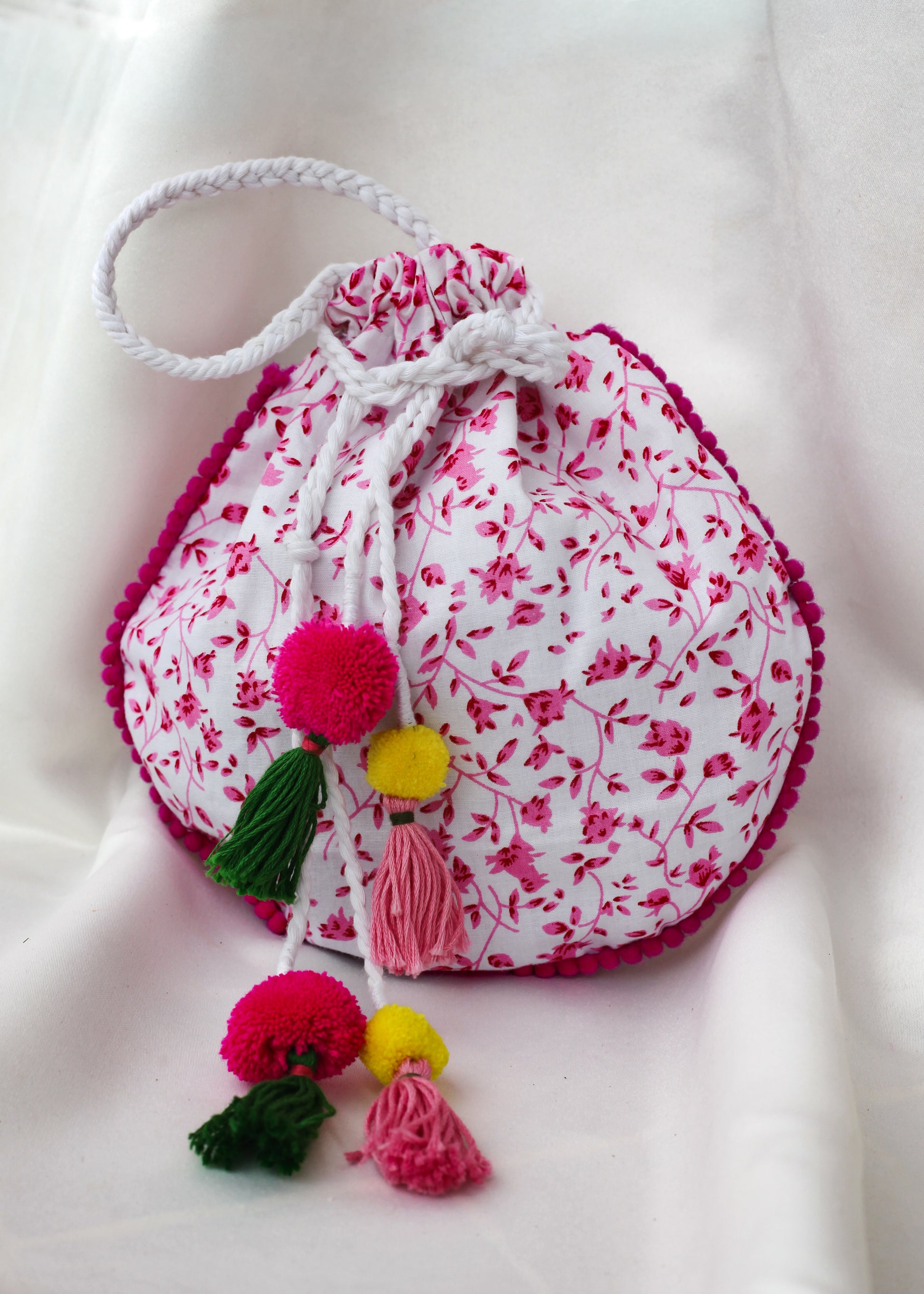 Drawstring bag with floral print, and colorful pom-poms on a white background