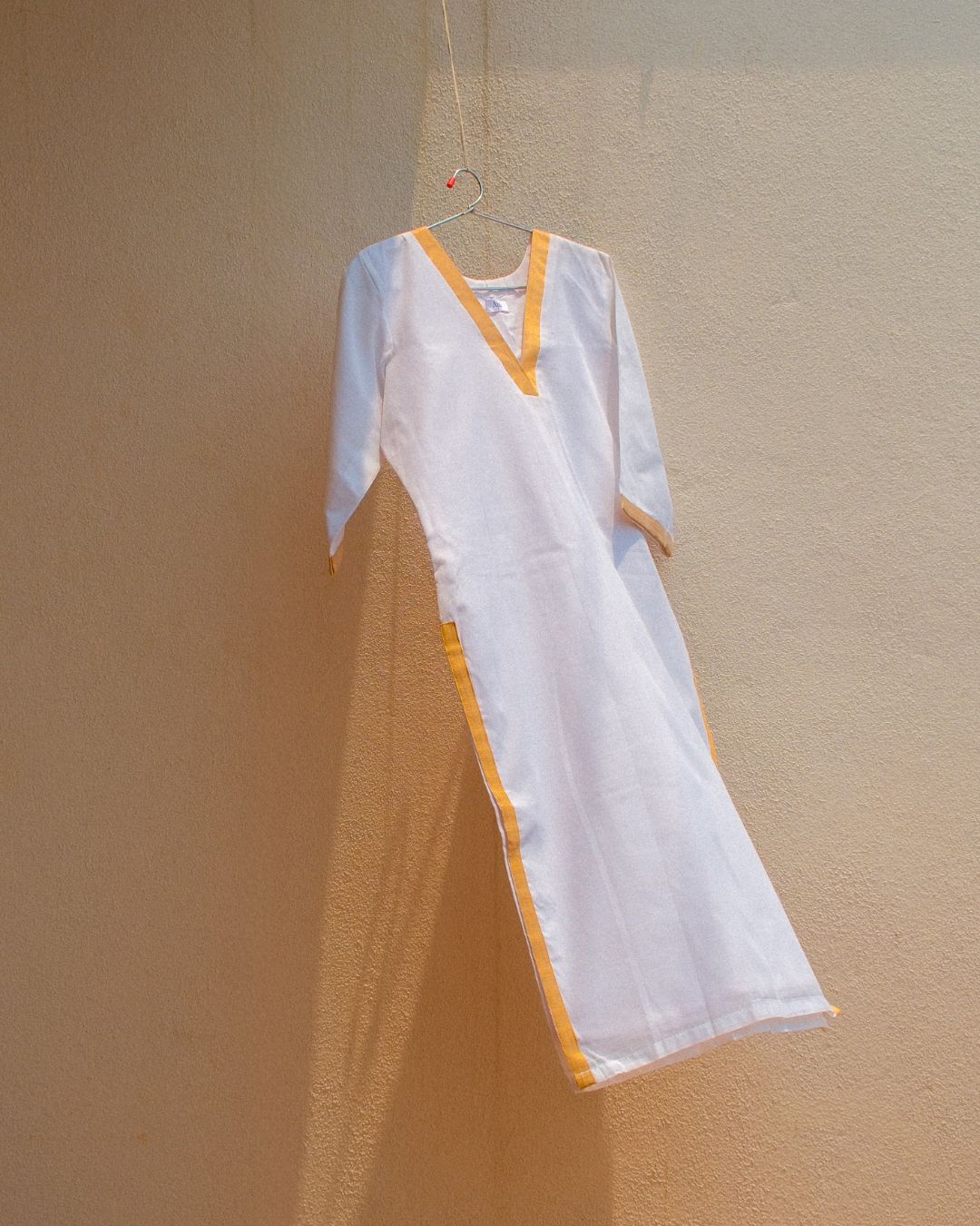 White cotton kurta with gold zari border hanging against a beige wall