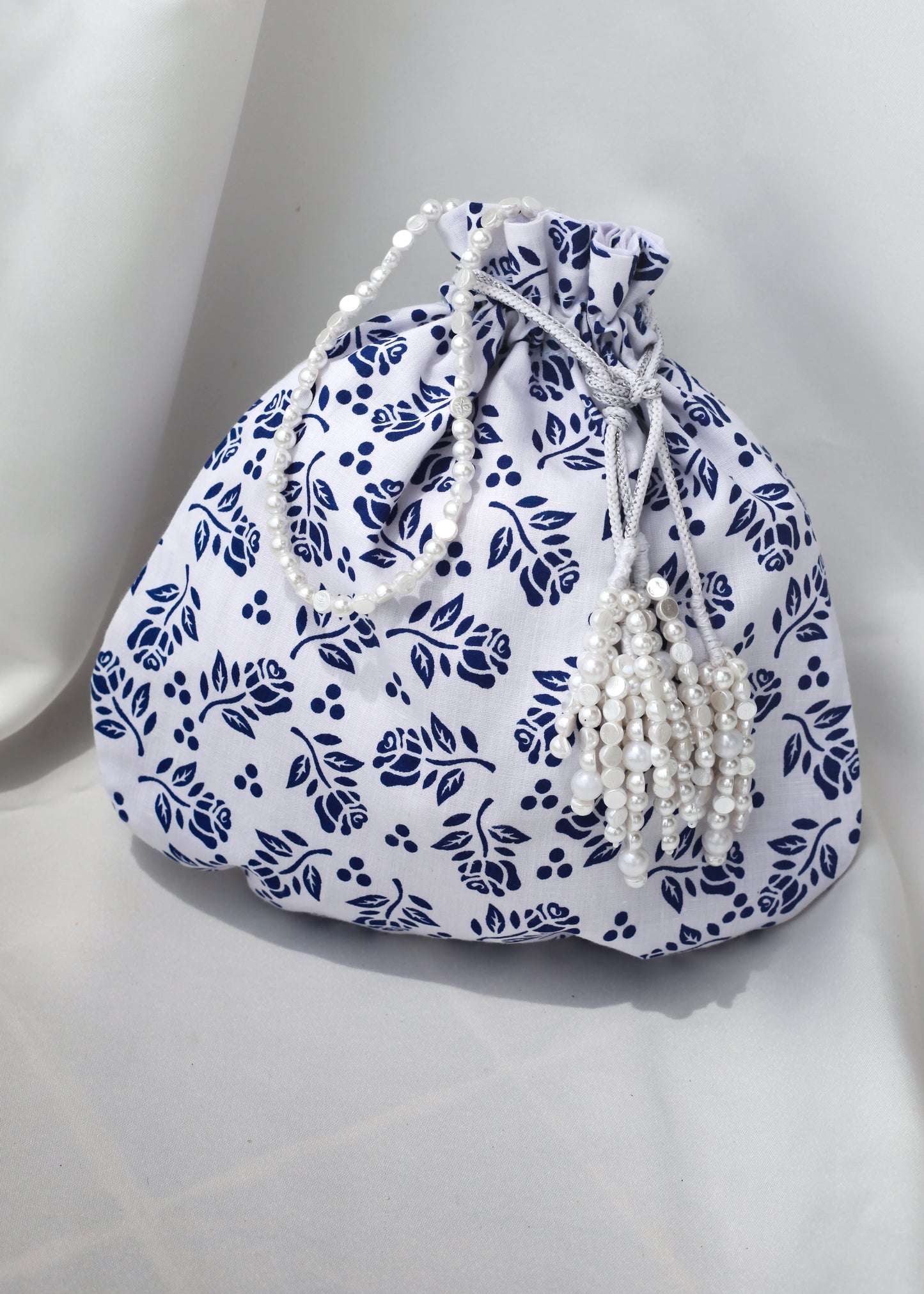 White drawstring bag with blue floral print and pearl strings on a white background