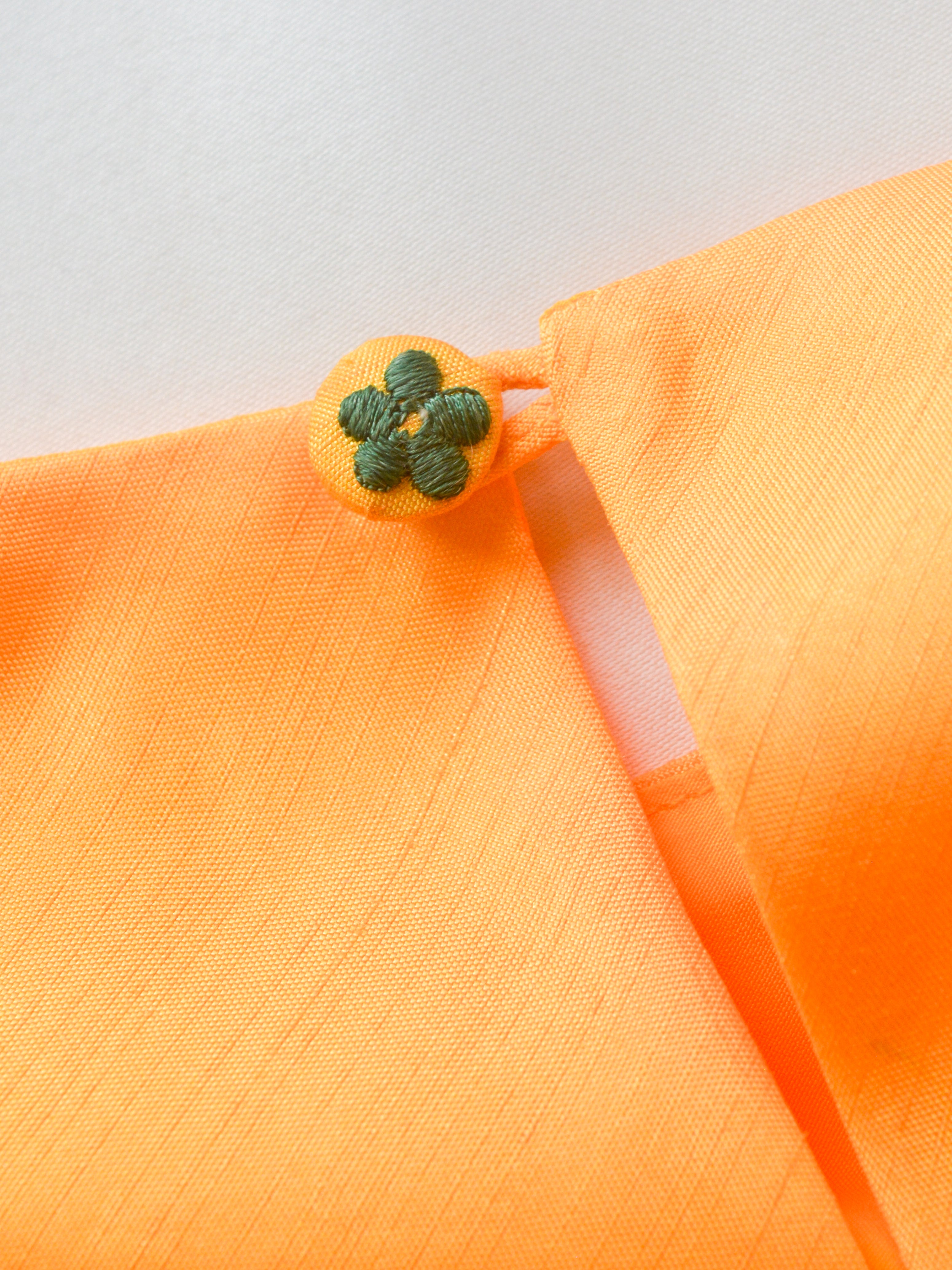 Close-up of the flower motif embroidered on fabric button on the back of the yellow muslin silk shevanti kurta.
