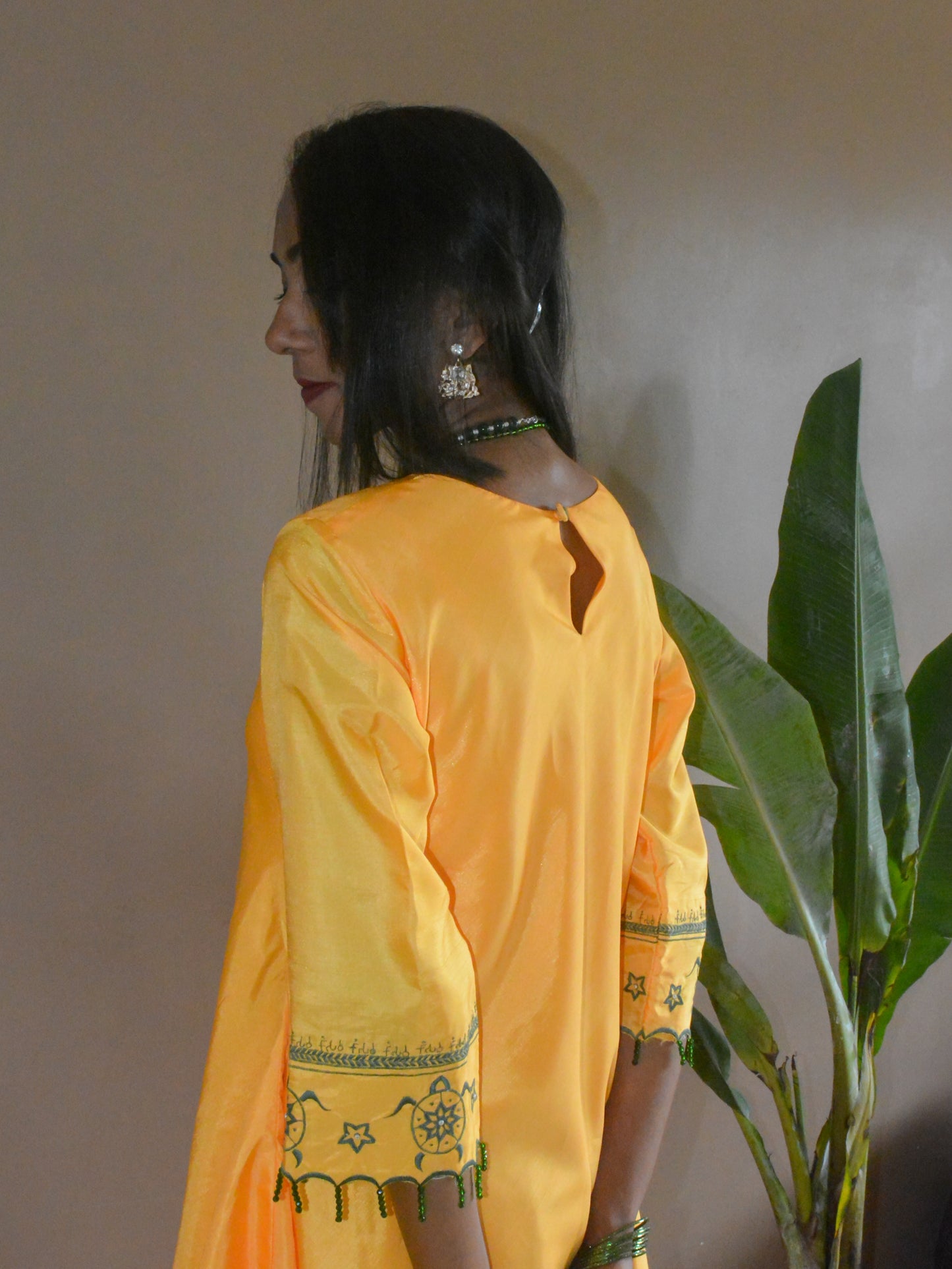 Back view of the shevanti kurta, showing the turtle motif embroidered on sleeves with green crystal hangings on scalloped hem.