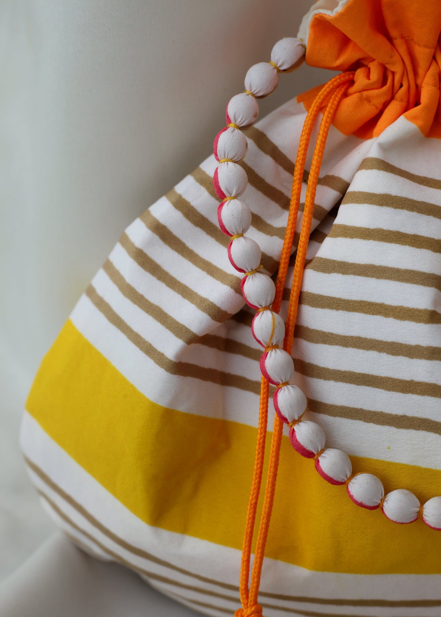 Striped bag with a drawstring featuring beaded handle and an orange drawstring.