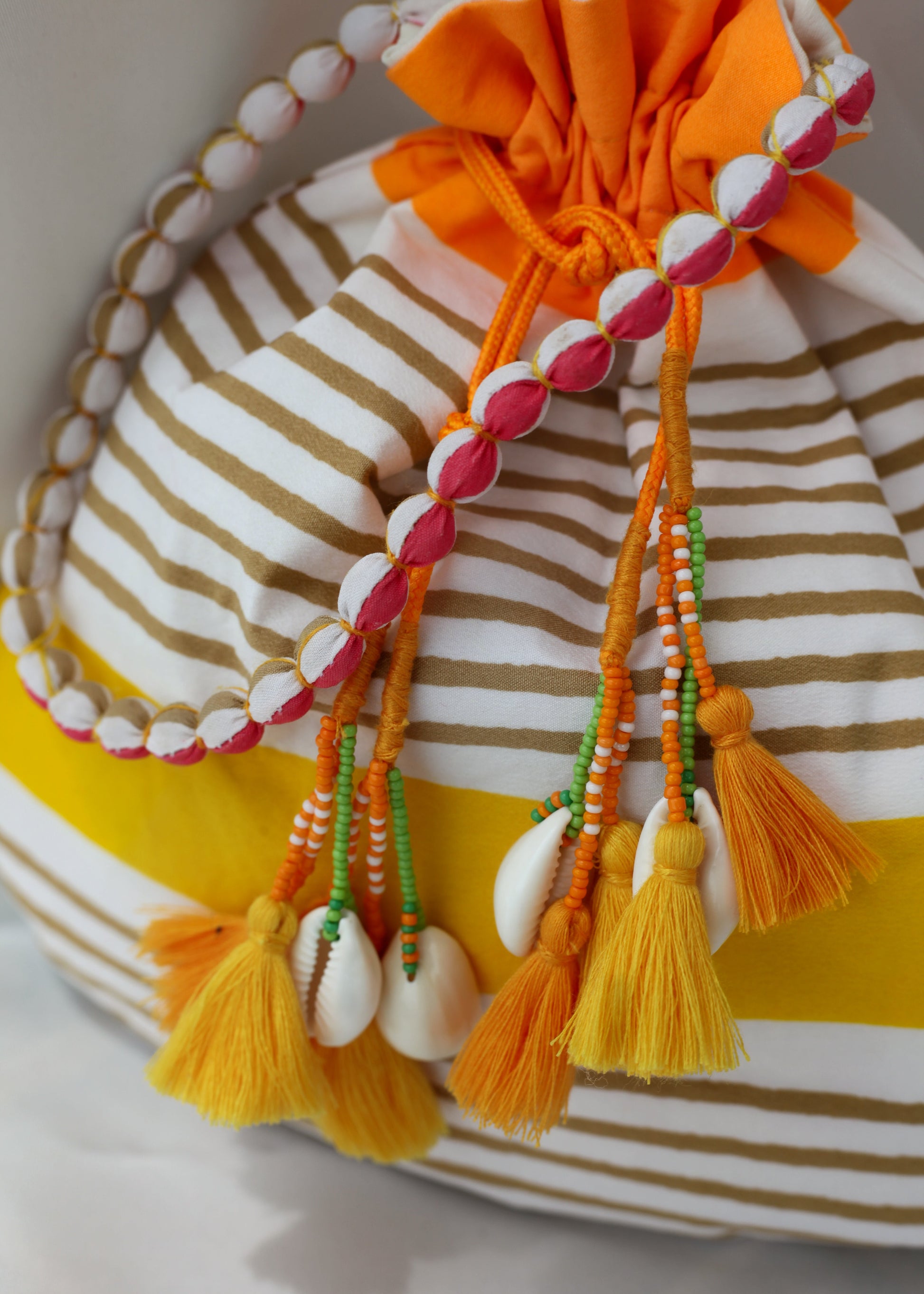 Drawstring bag with colorful tassels, shells, and beads on a white background