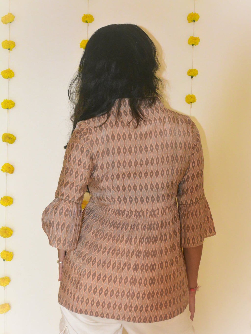 Woman wearing a beige printed musli-silk tunic with a neutral background and yellow decorative flowers.