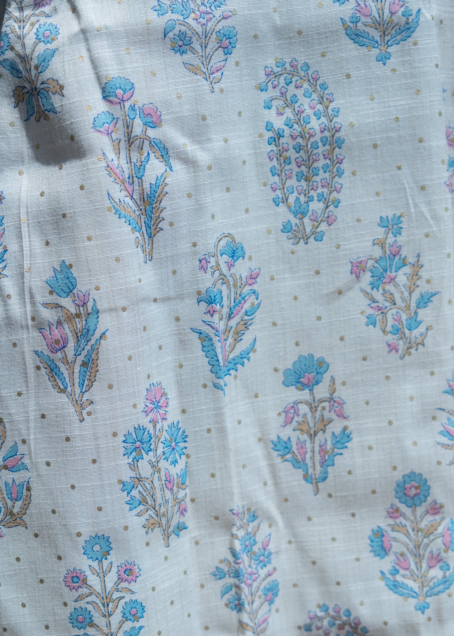 Close-up of pastel floral print on slub cotton fabric with small gold dot details.
