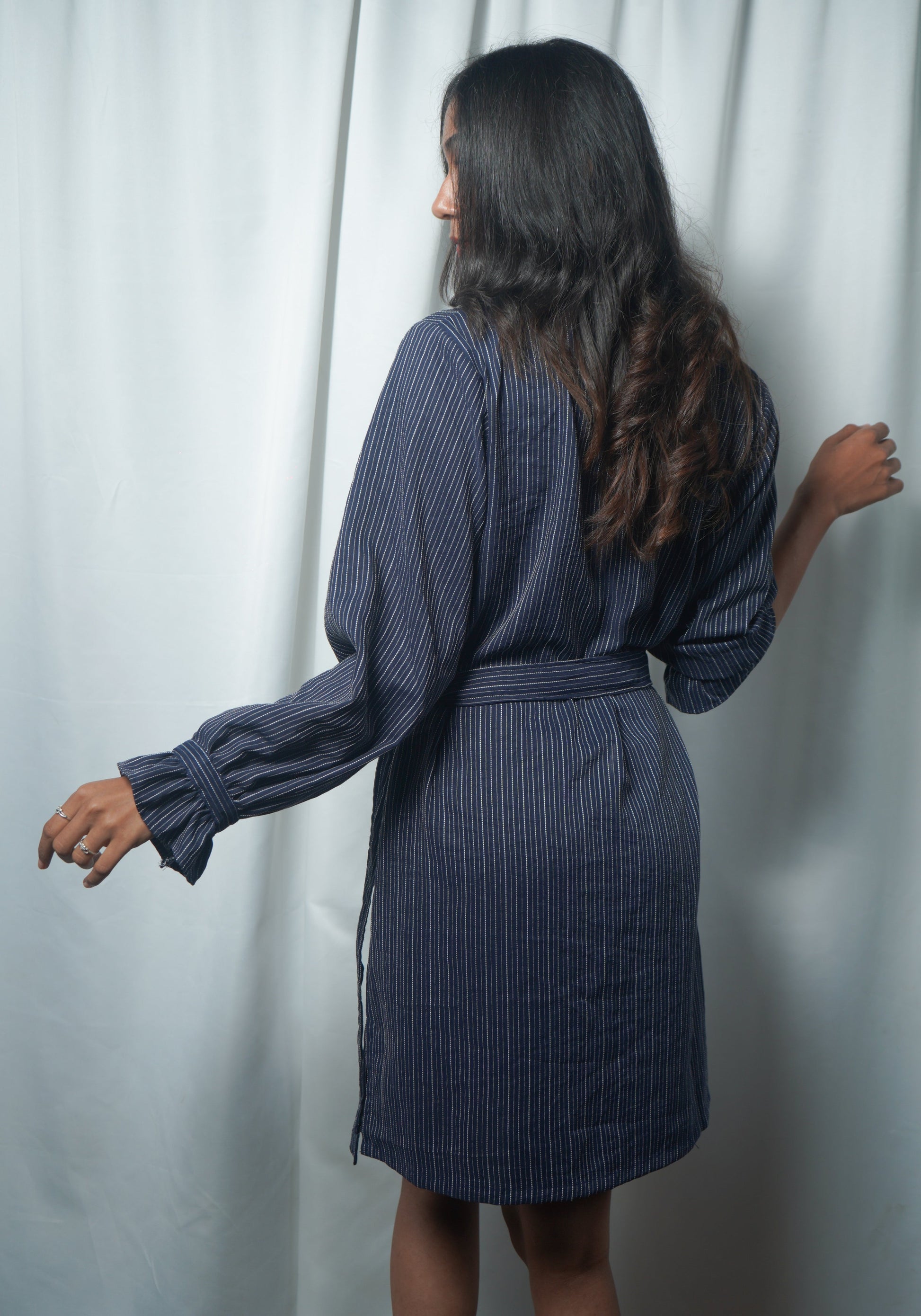 Woman wearing a blue pinstripe dress against a white curtain