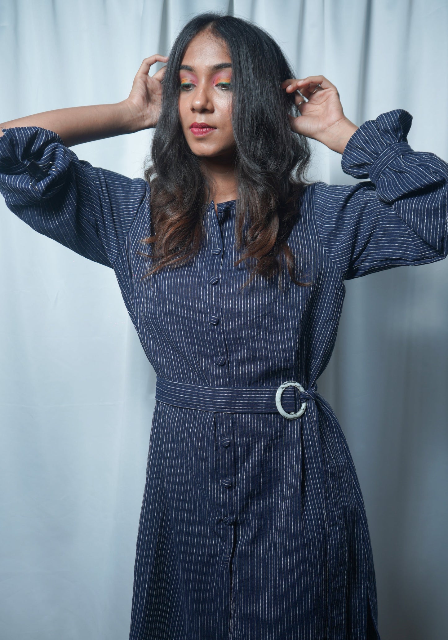 Woman wearing a blue pinstripe dress with a belt against a light background