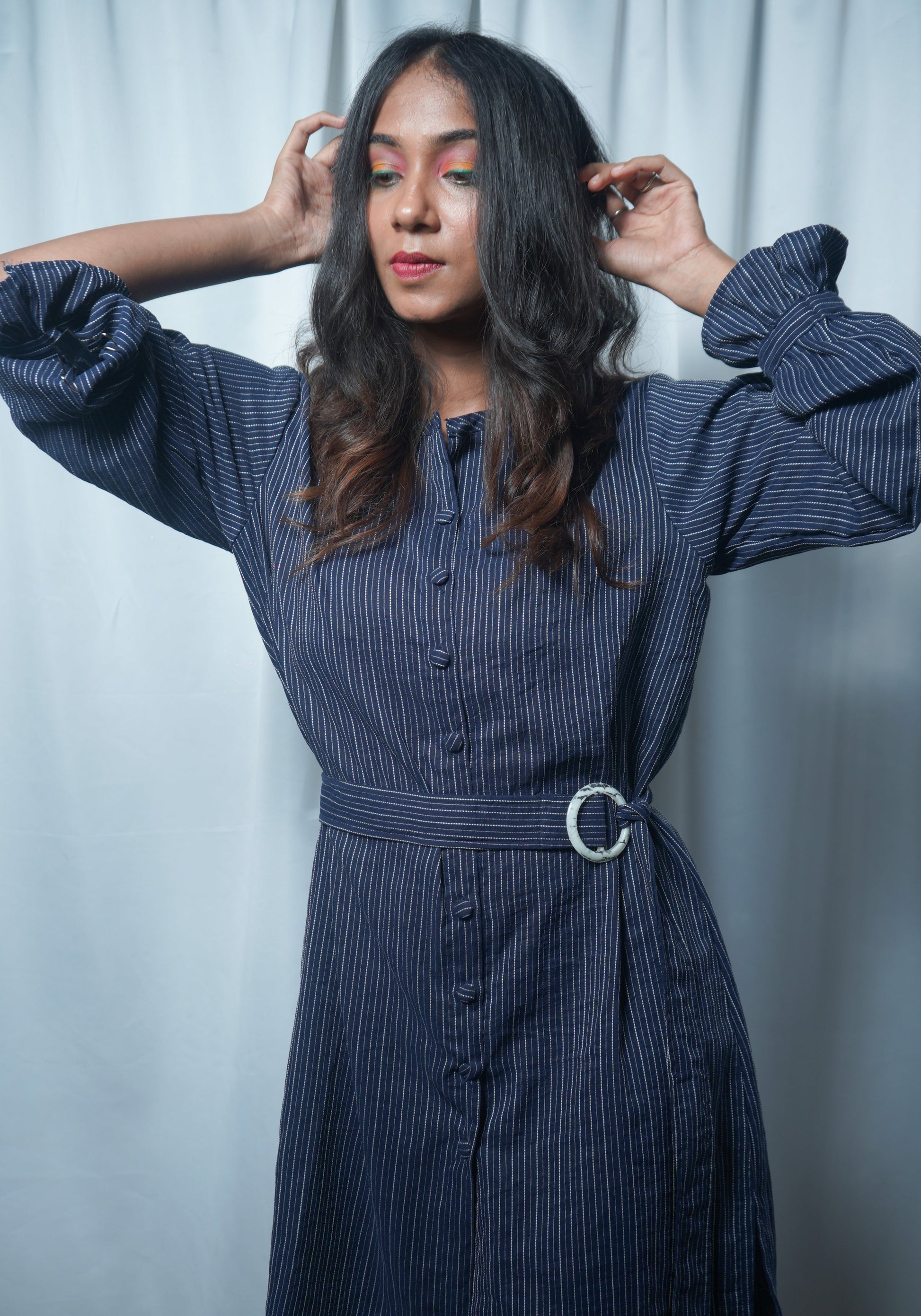 Woman wearing a blue pinstripe dress with a belt against a light background