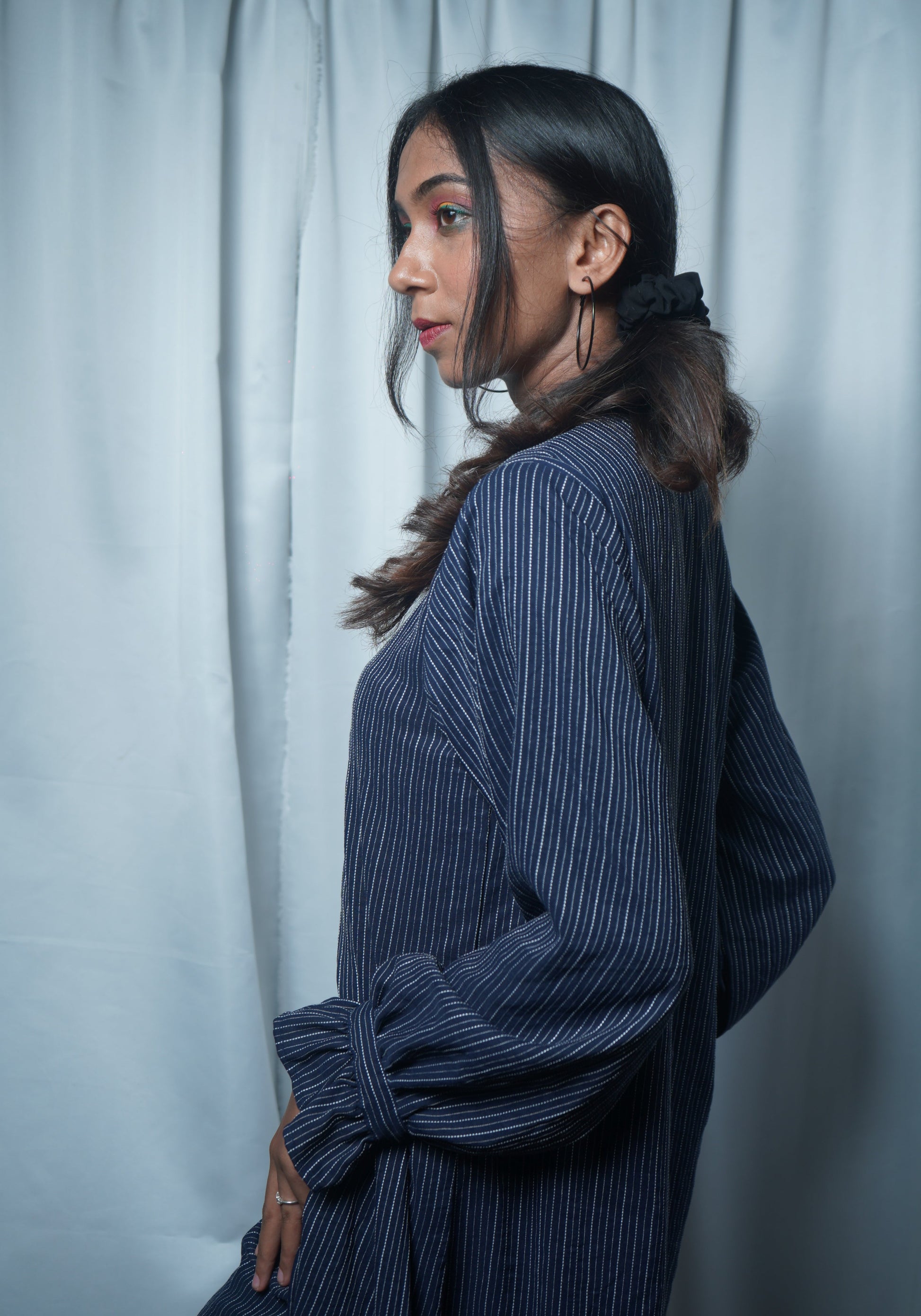Woman wearing a blue pinstripe dress against a light gray curtain background