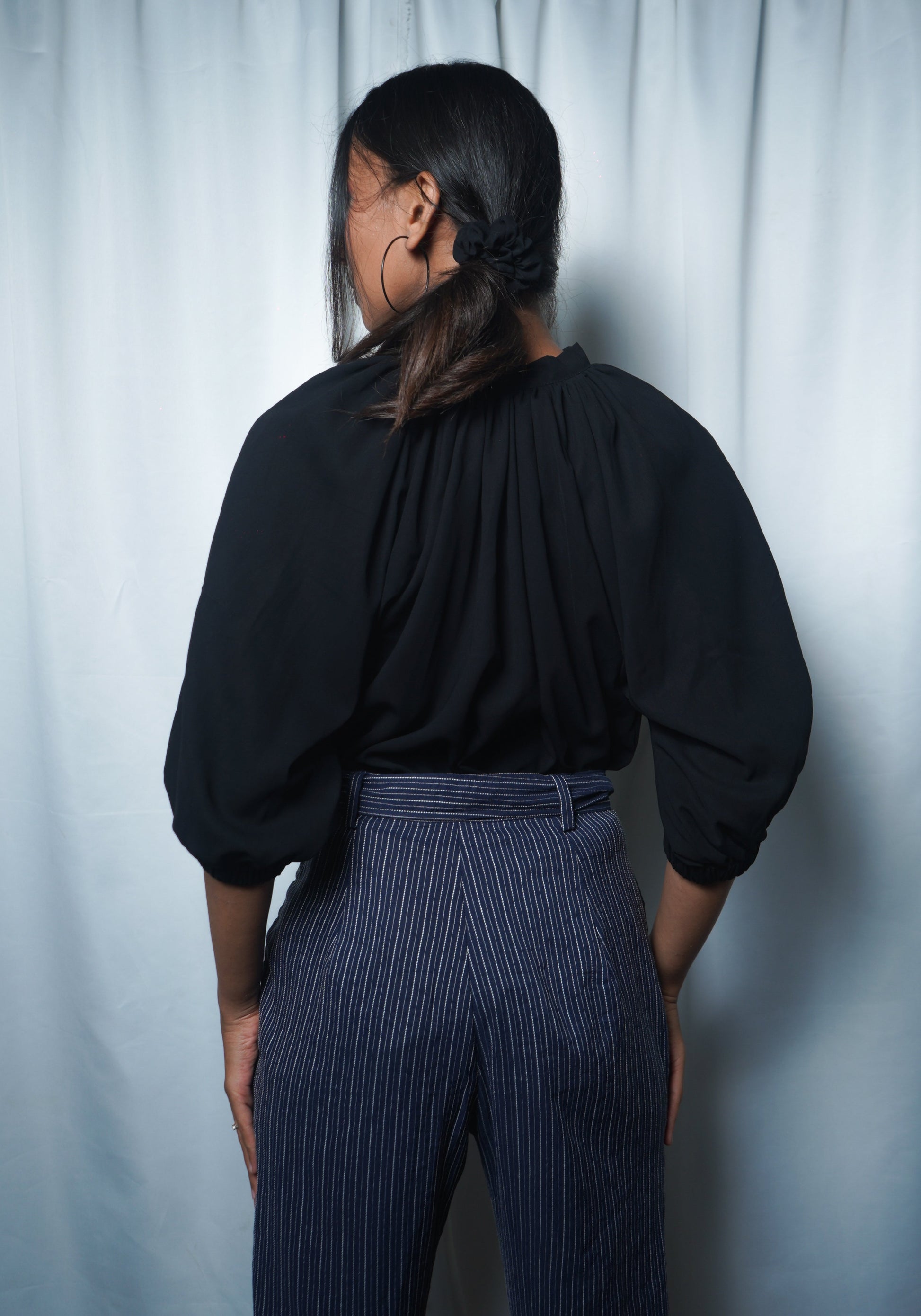 Person wearing a black top and blue striped pants against a white curtain background