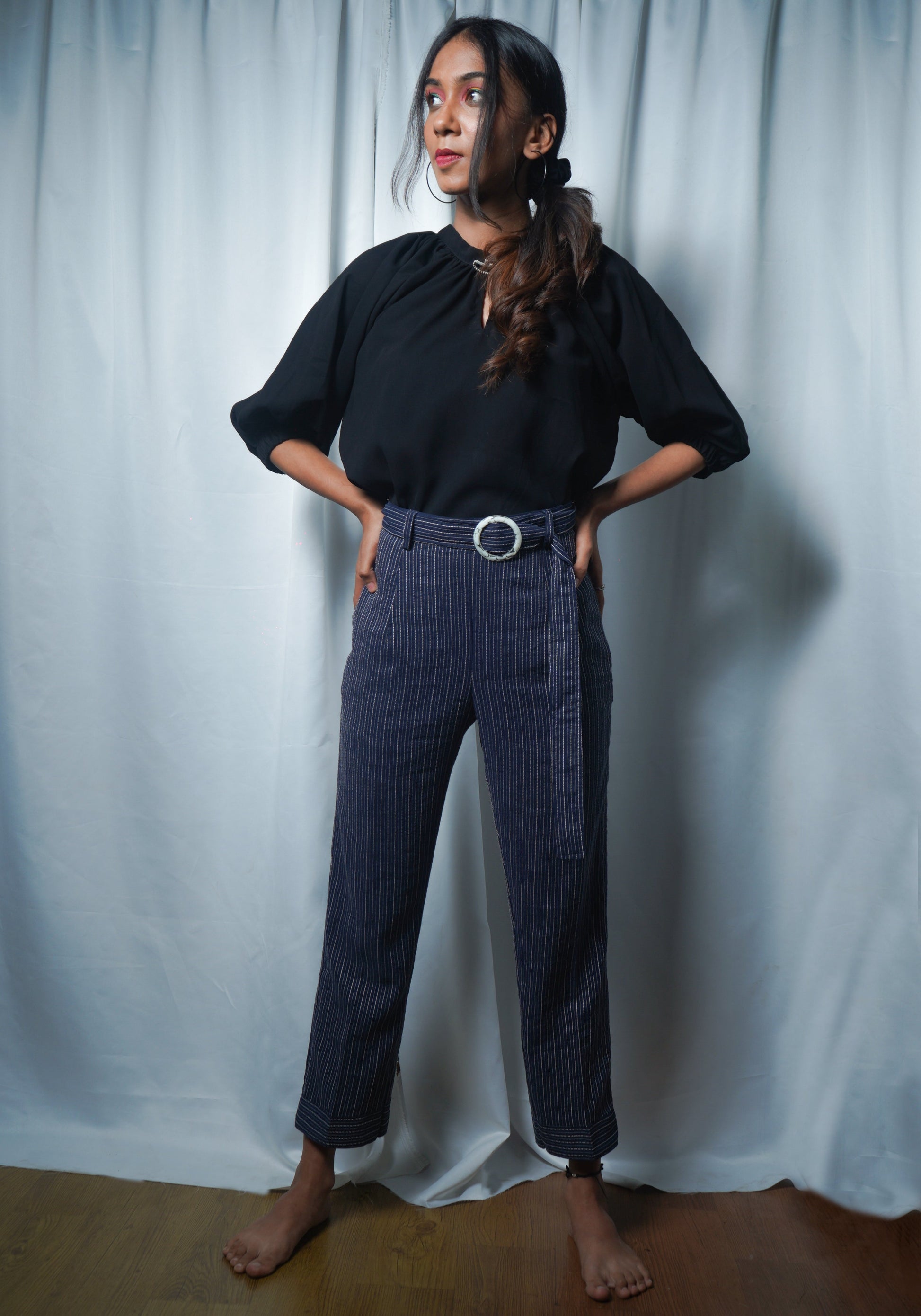 Woman wearing a black top and blue striped pants against a white curtain background
