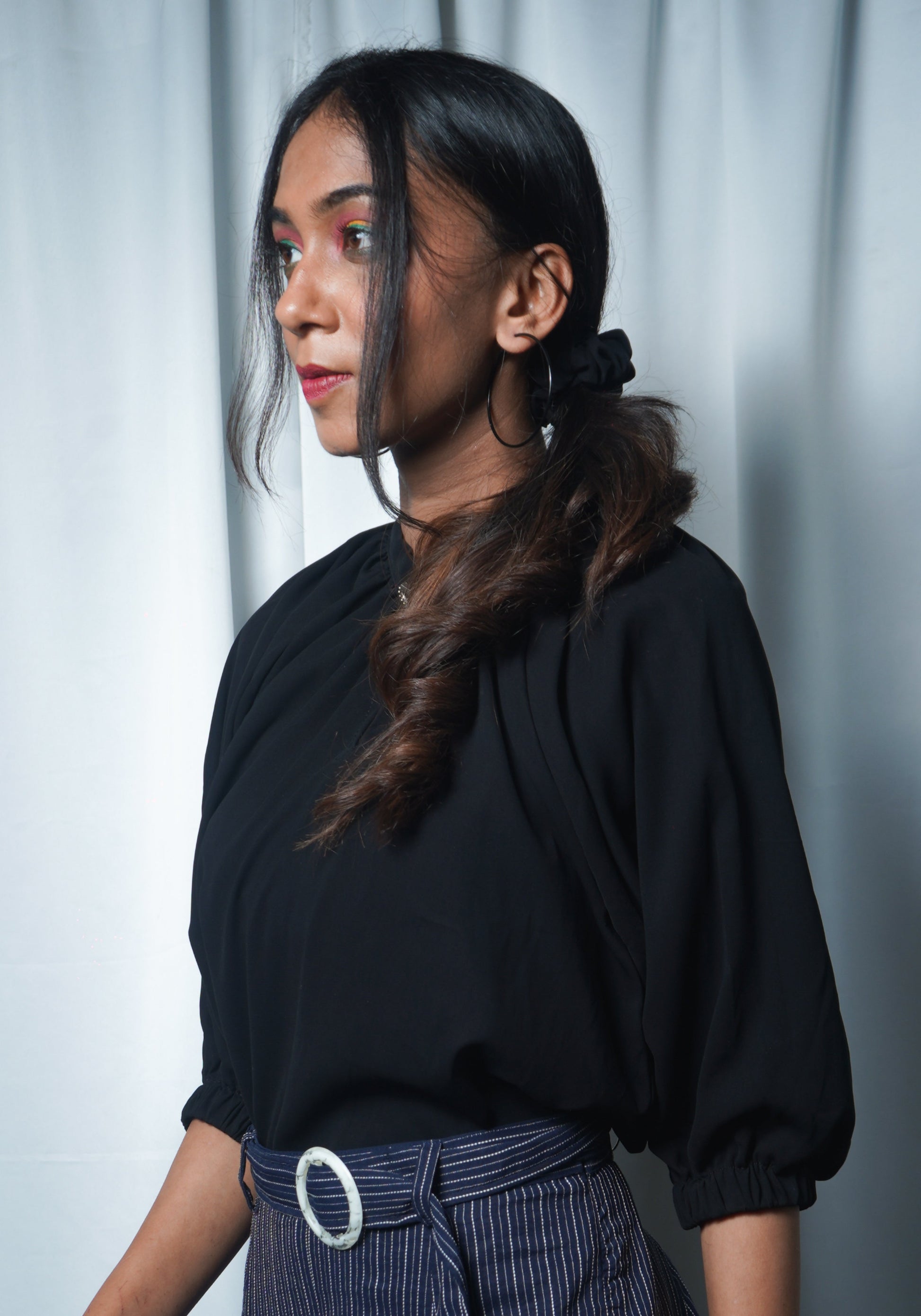 Woman wearing a black top with puffed sleeves against a light white curtain background