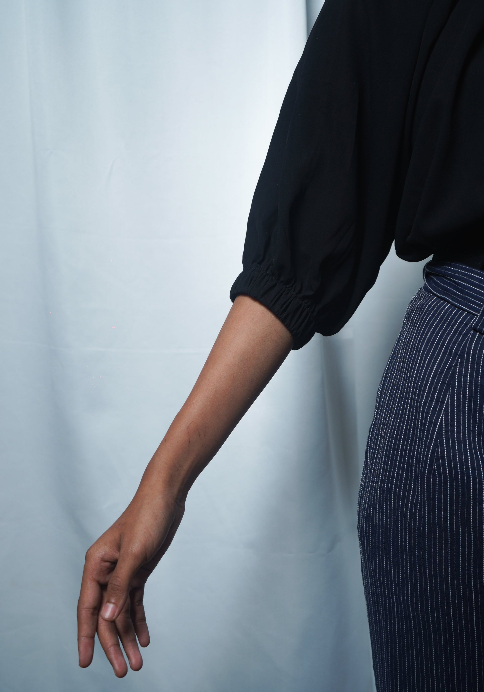 Person wearing a black long-sleeve top and striped pants against a light white background