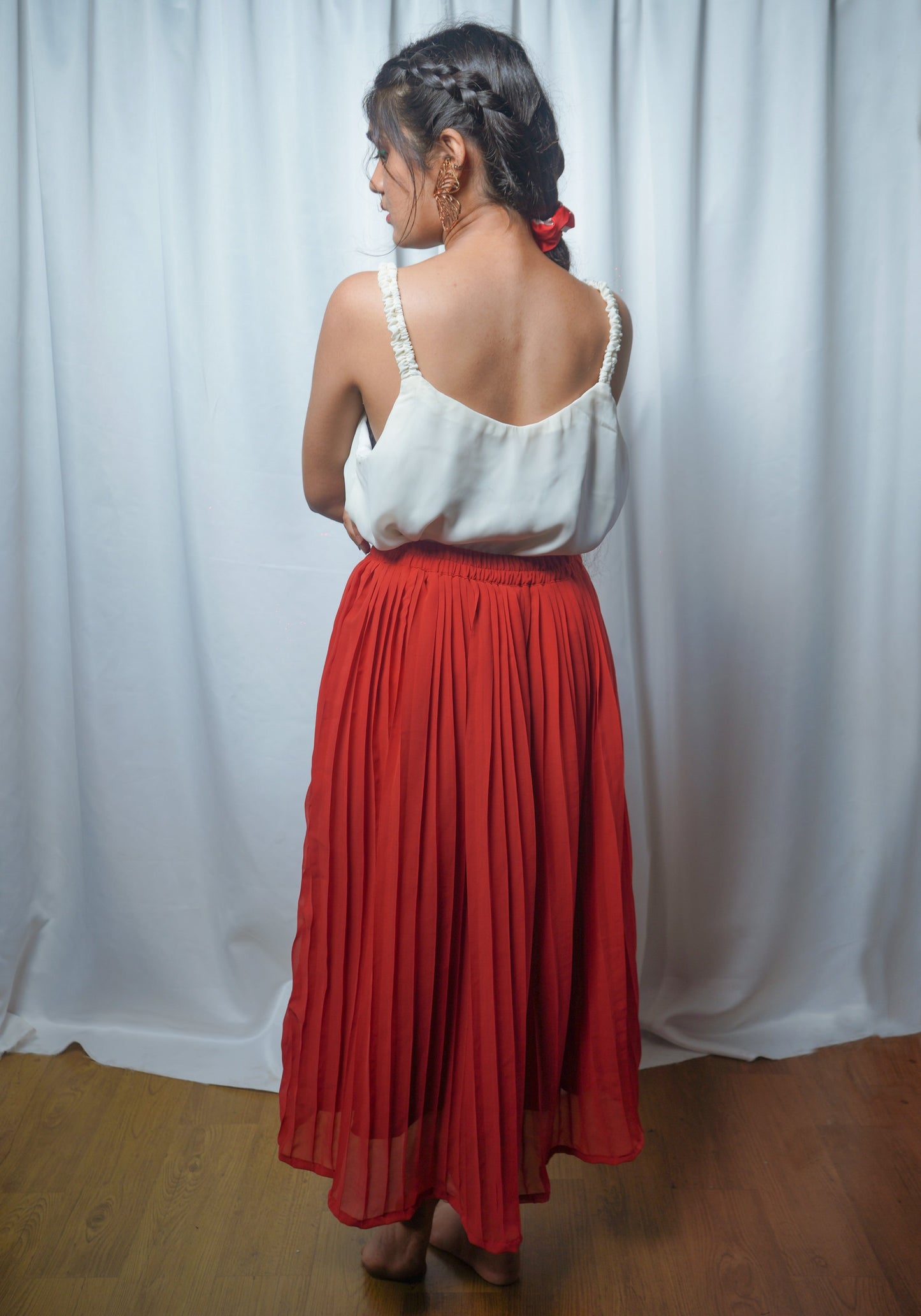Woman wearing a white top and red skirt standing against a white curtain.