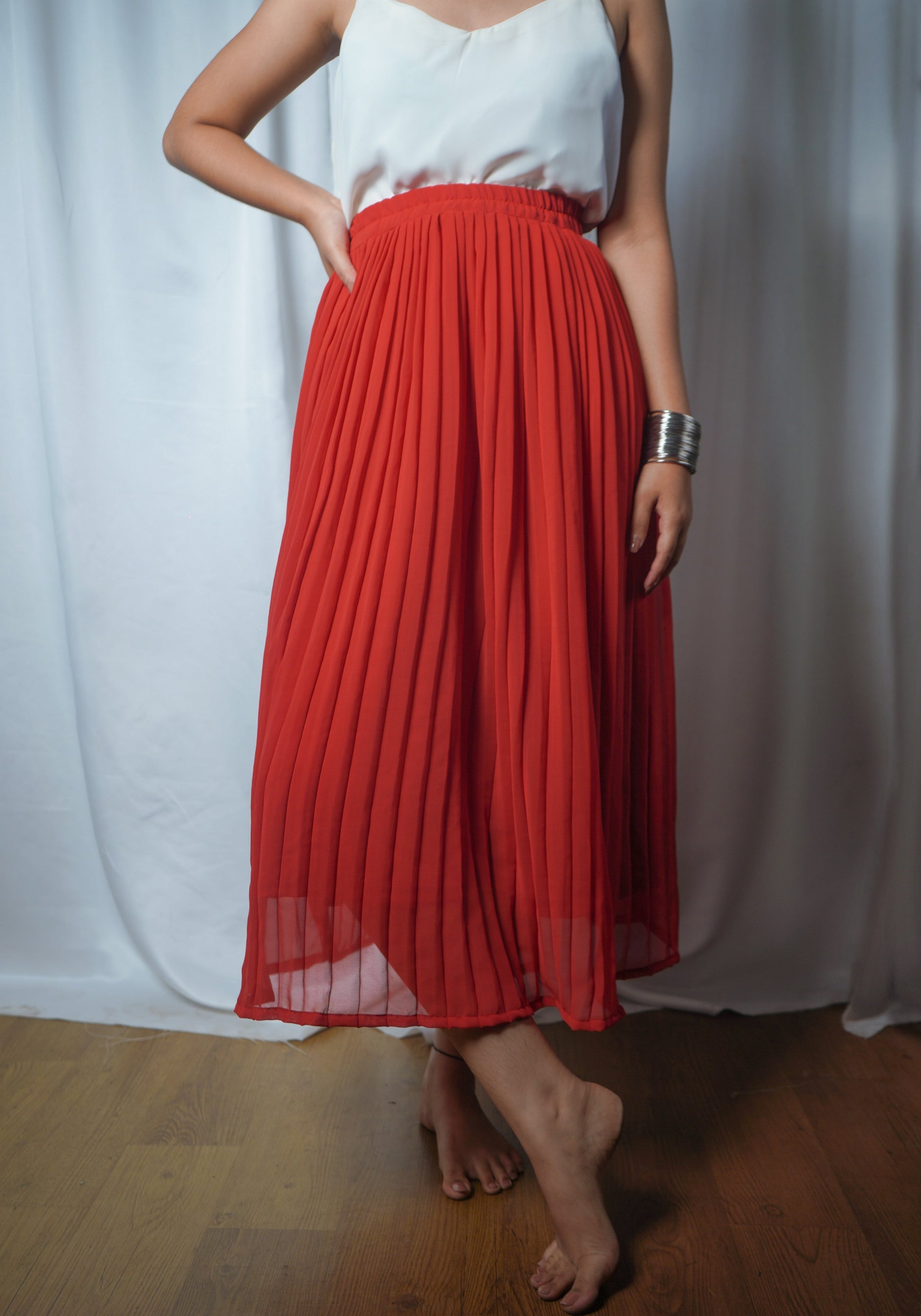 Person wearing a white top and red pleated skirt against a white curtain background