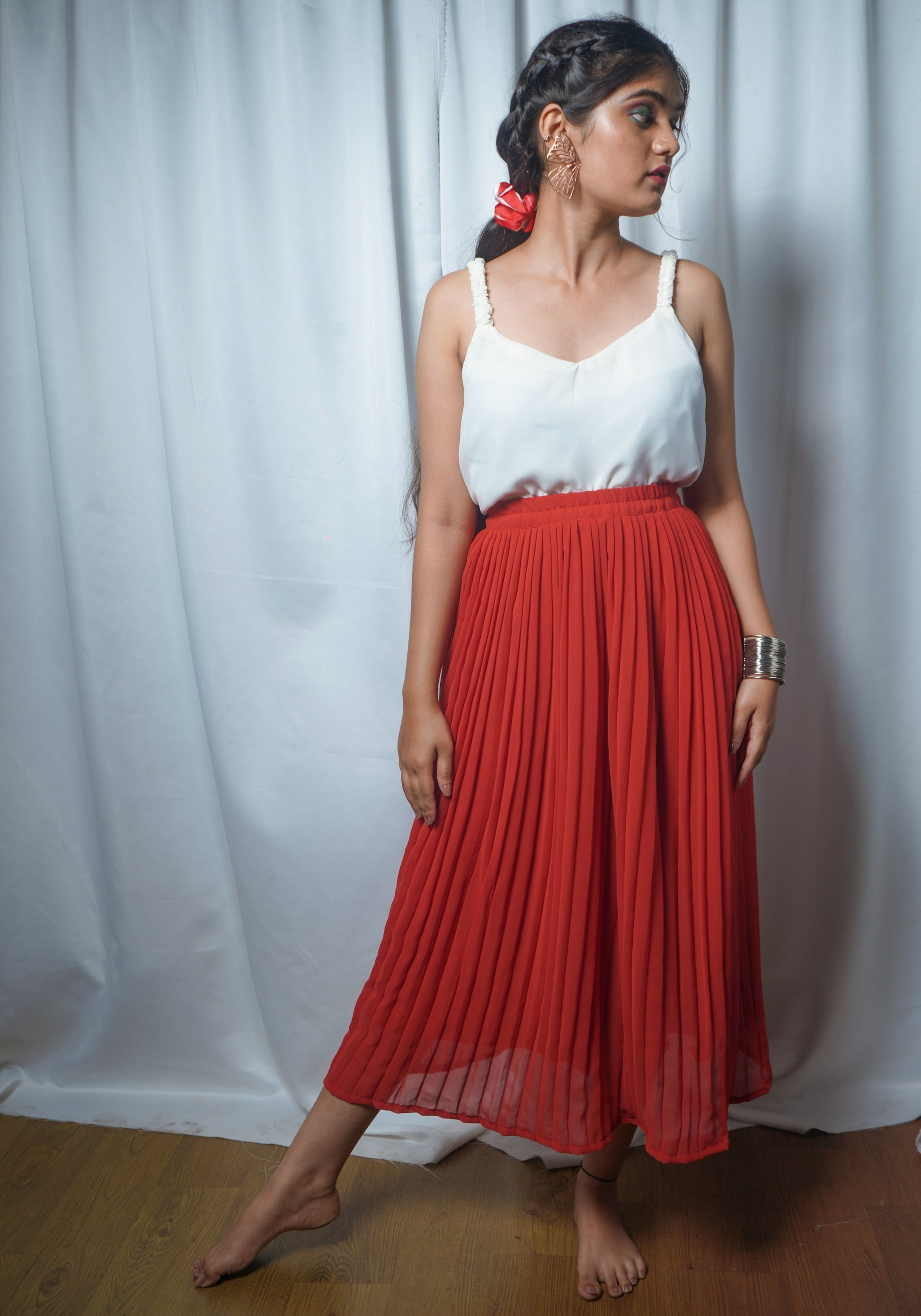 Woman wearing a white top and red pleated skirt against a white curtain background