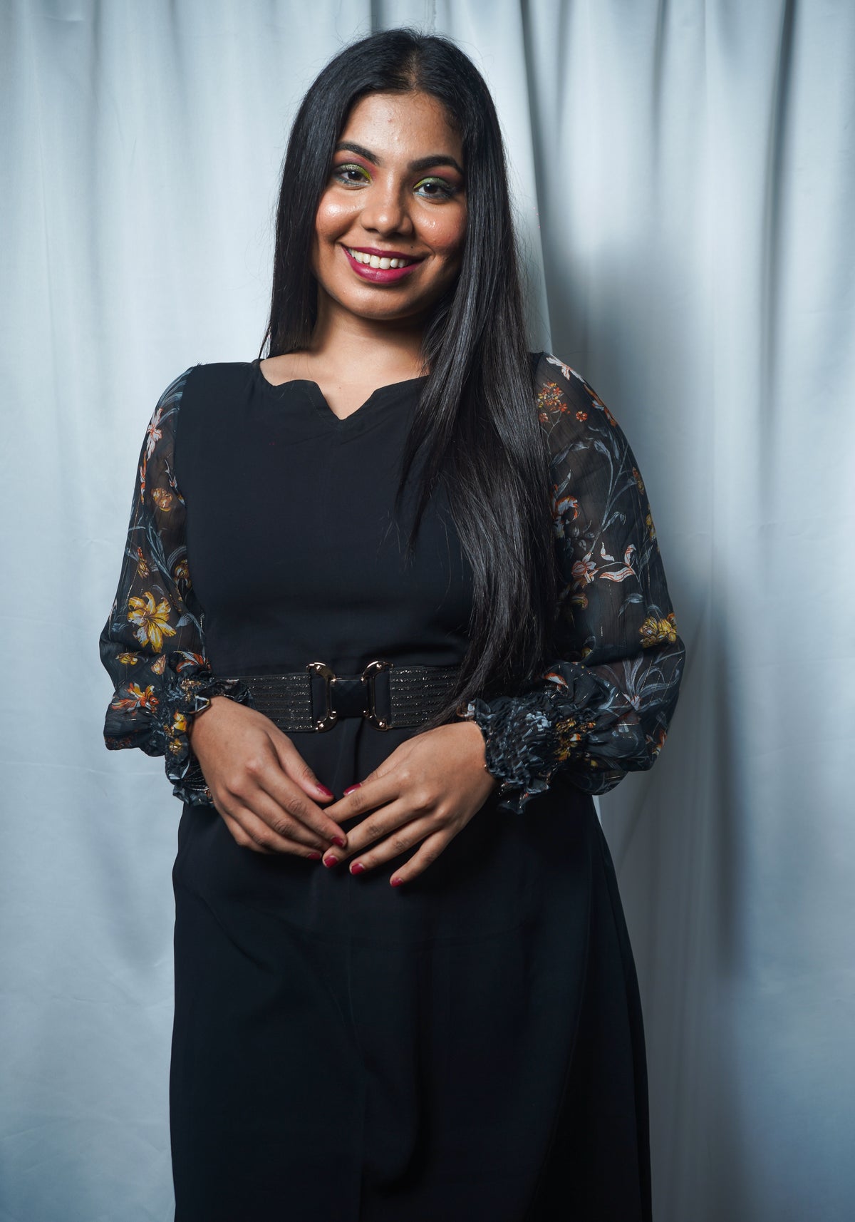 A woman wearing an asymmetrical dress with floral printed long sleeves and a scoop neckline in a charcoal black color styled with waist belt.